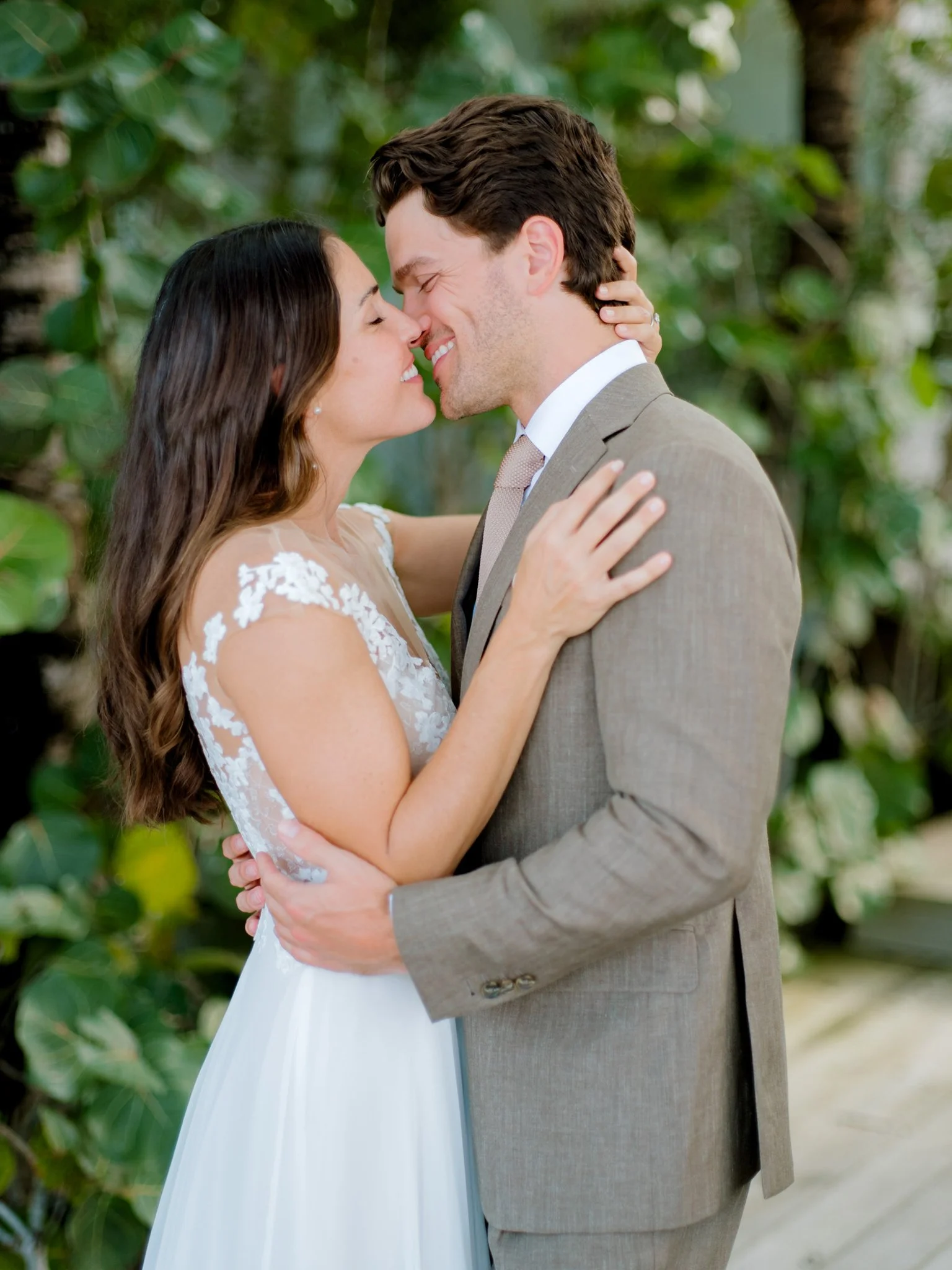 A bride and groom embrace and smile with their foreheads touching in a lush green setting, dressed in wedding attire at The Other Side Hotel Eleuthera during a luxury Bahamas destination wedding.