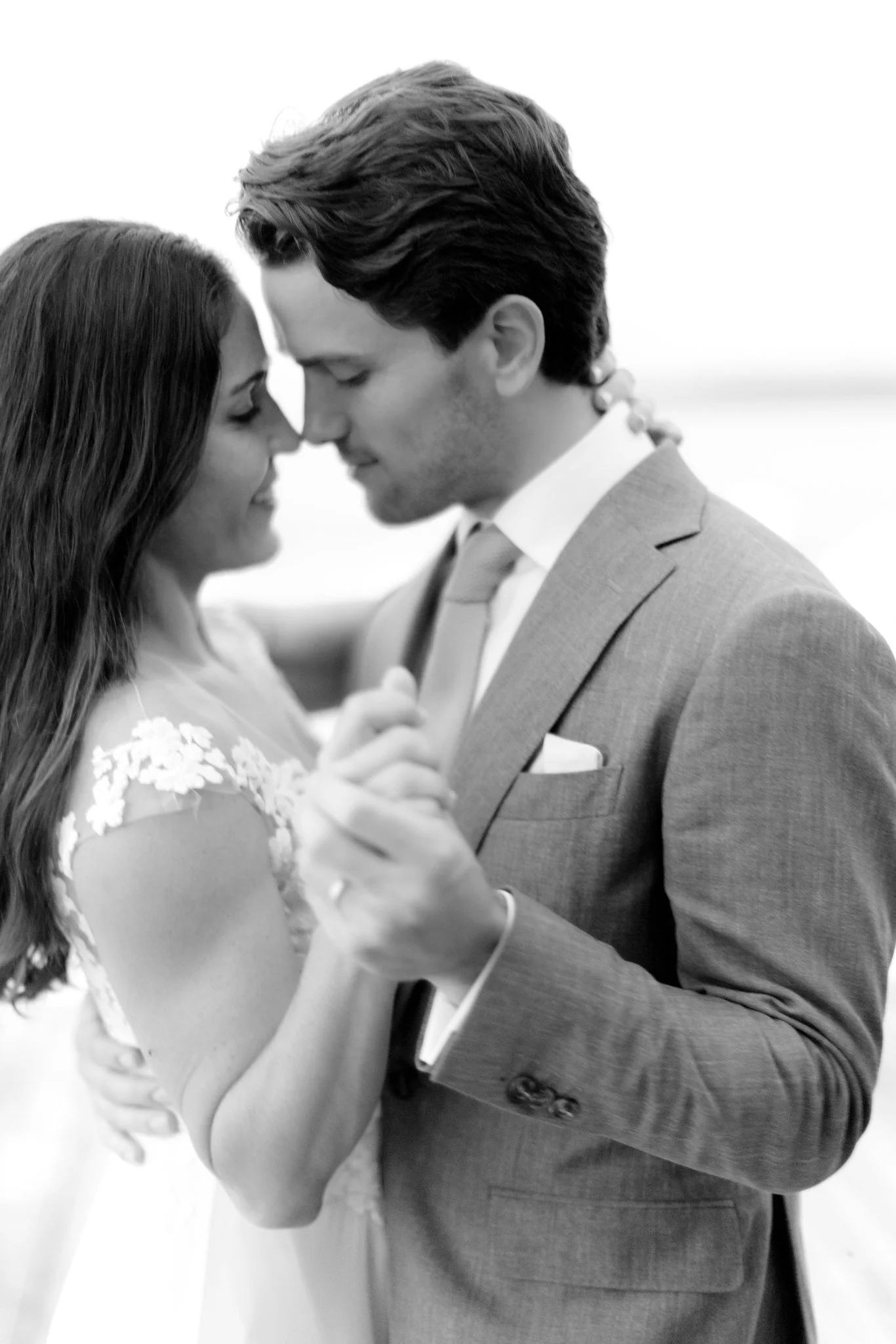 A black-and-white photo of a romantic moment between a bride and groom, with their foreheads touching and eyes closed, holding hands in a close embrace at The Other Side Hotel Eleuthera during a luxury Bahamas destination wedding.