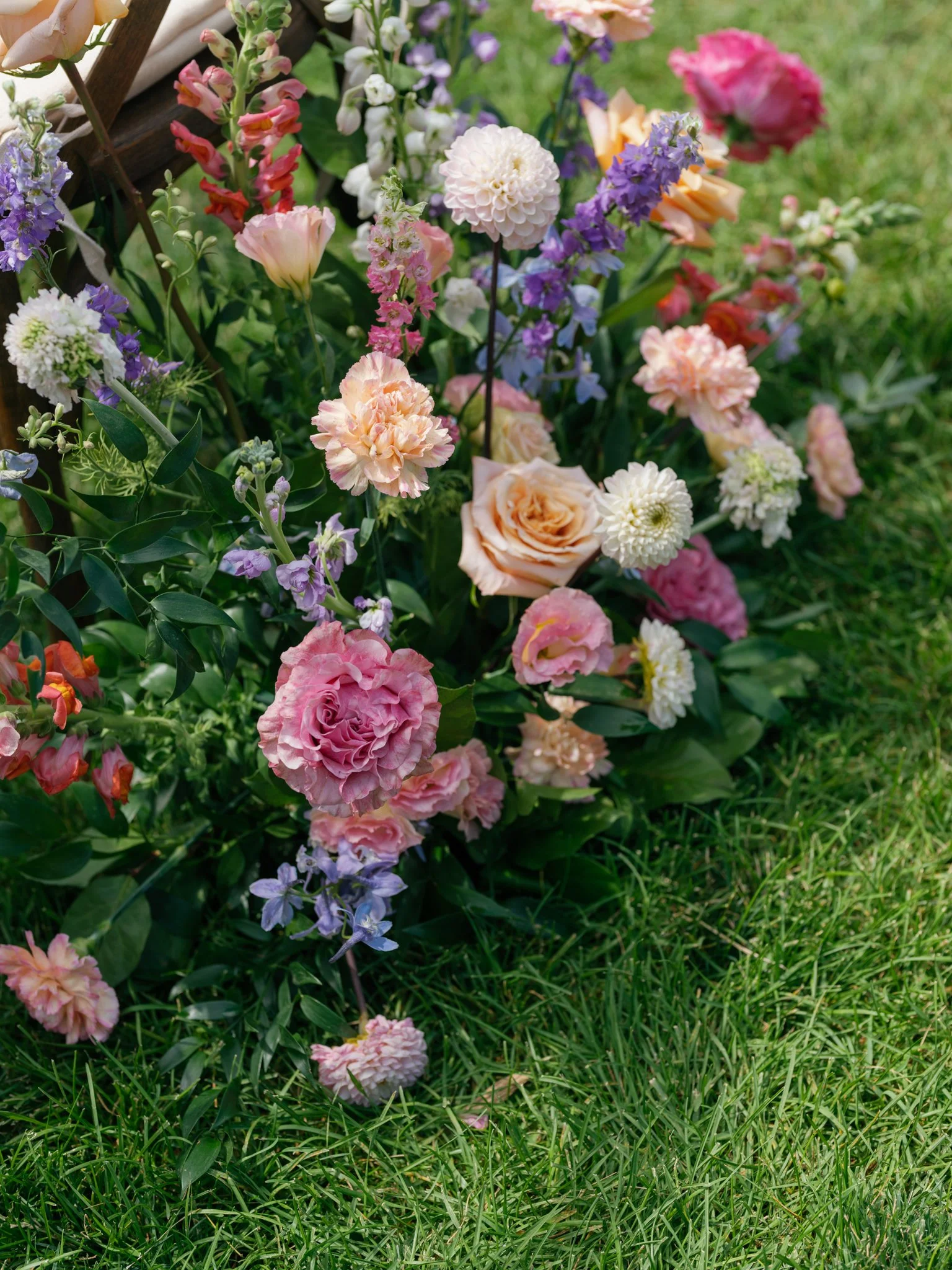 A colorful array of blooming flowers including pink, purple, peach, and white blossoms in a garden bed with green grass in the background at Elk Point wedding in Coeur d’Alene.