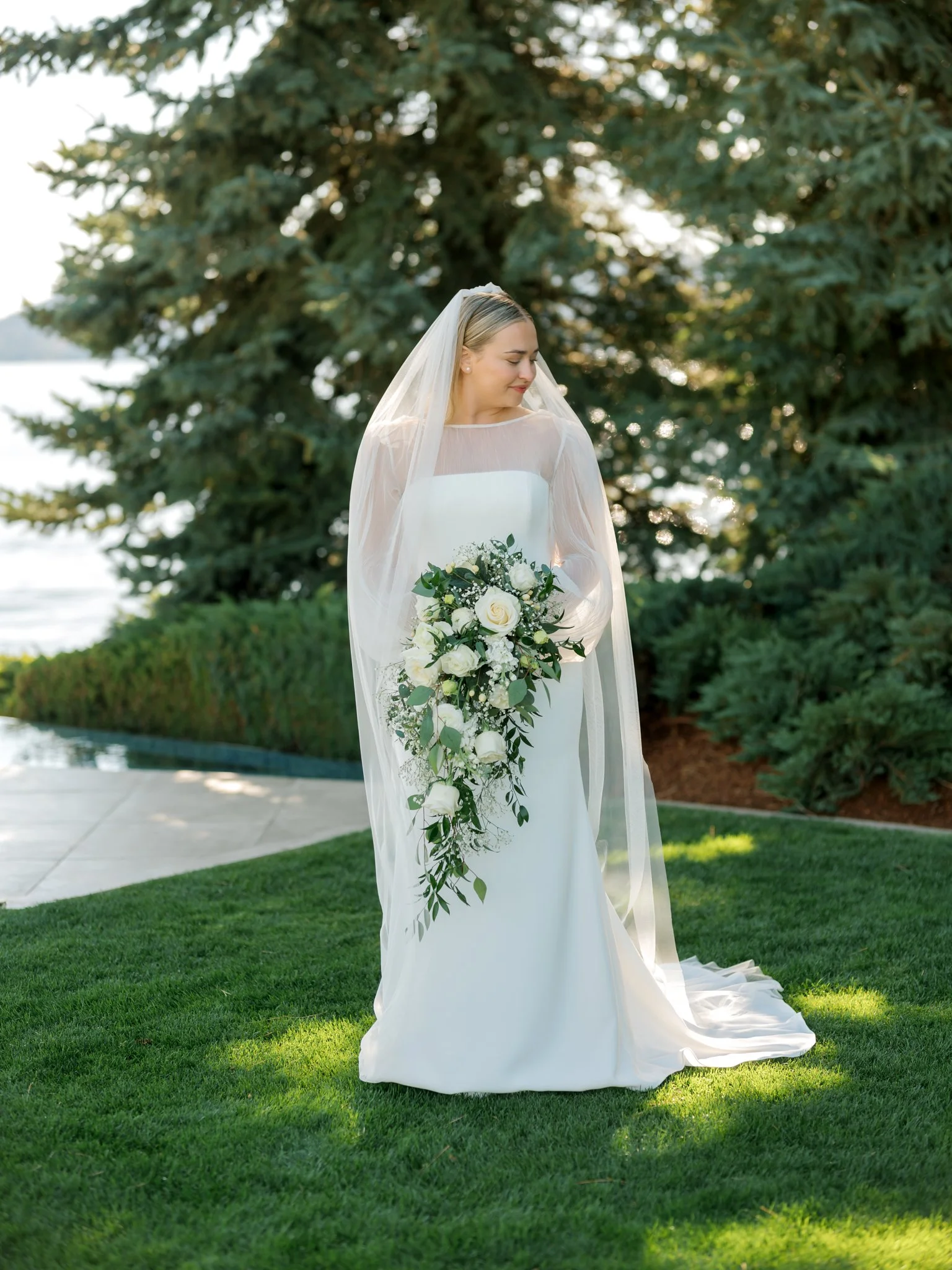 Bride standing on the lawn with a cascading white bouquet and long veil during a summer wedding at the Hagadone Event Center.
