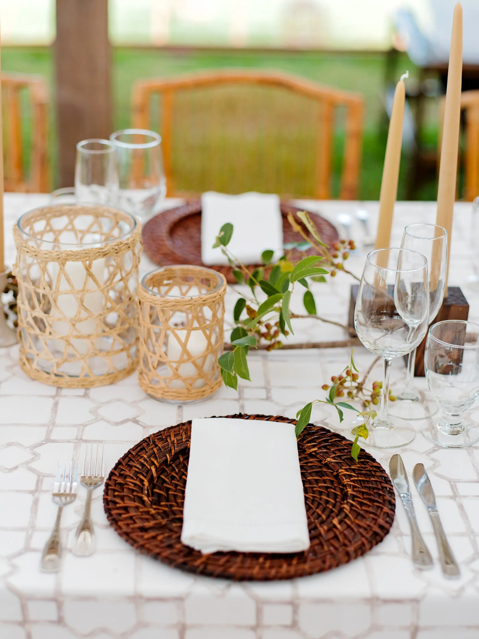 Elegant outdoor dining table set with wicker plates, cloth napkins, glassware, and candle lanterns, decorated with greenery at The Other Side Hotel Eleuthera during a luxury Bahamas destination wedding.