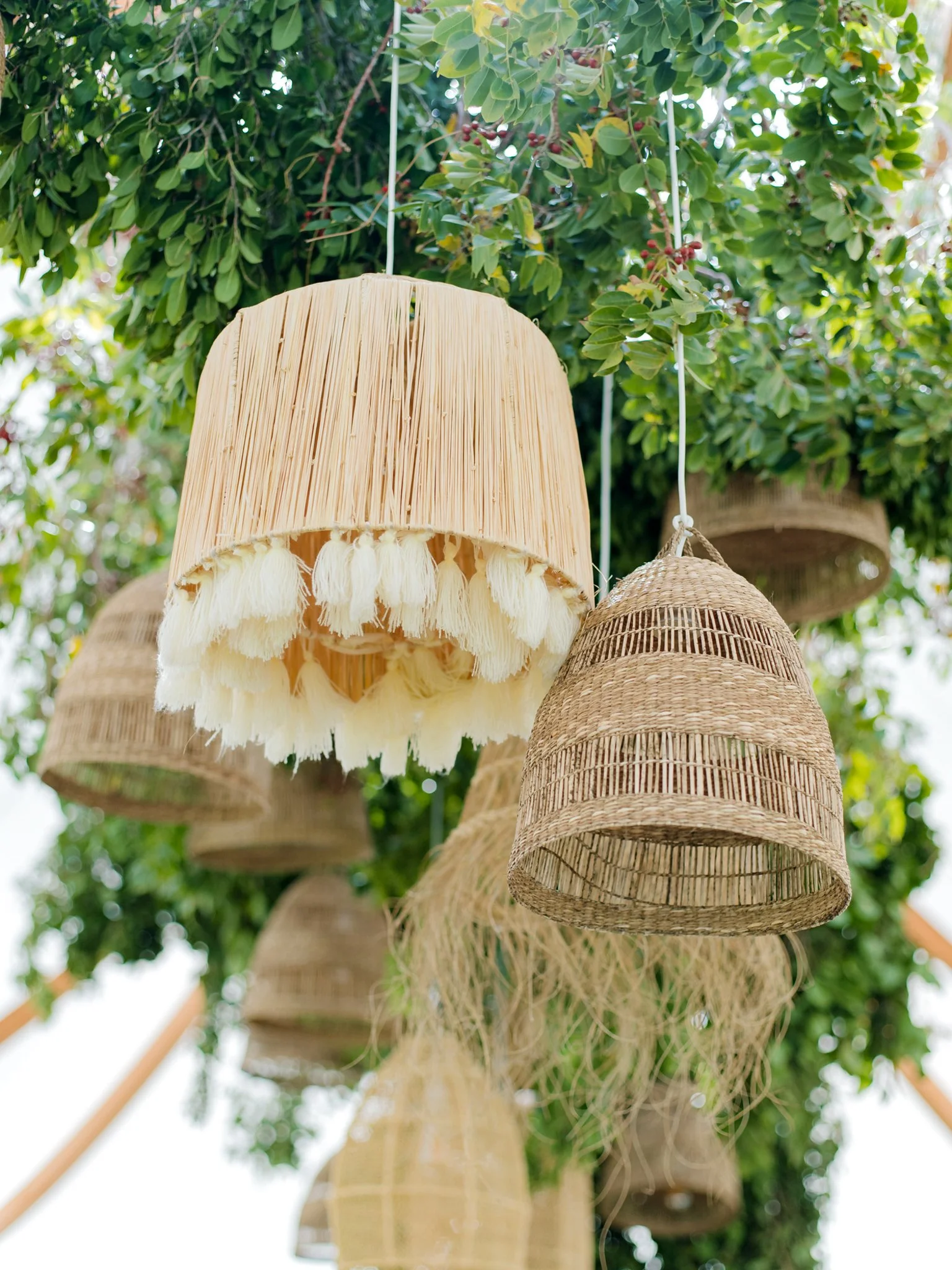 Hanging woven and fabric lampshades in natural colors under a tree with green leaves at The Other Side Hotel Eleuthera during a luxury Bahamas destination wedding.