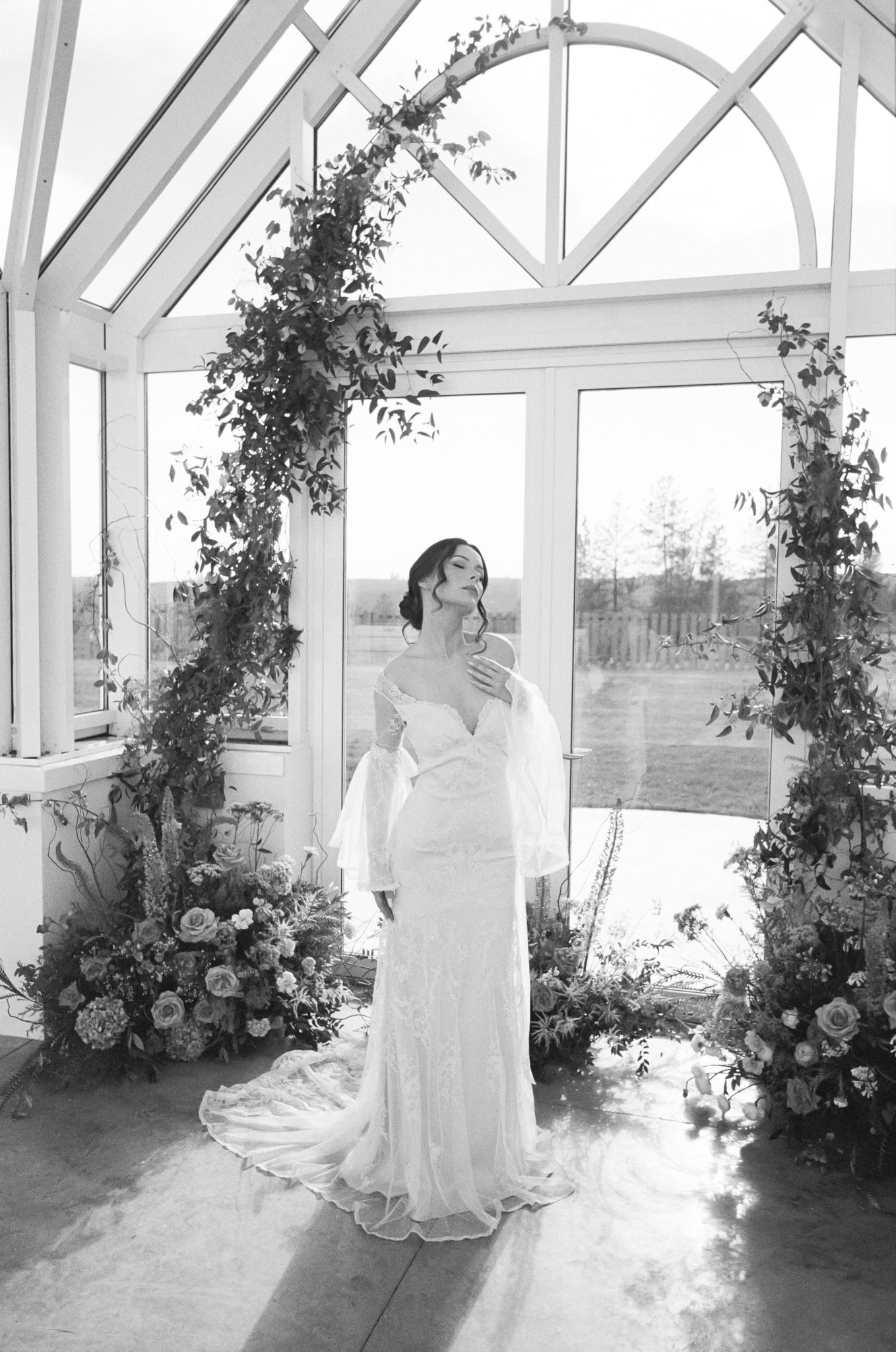 A woman in a wedding dress standing inside a glass greenhouse with floral decorations at Greenhouse on Harvard near Spokane, Washington.