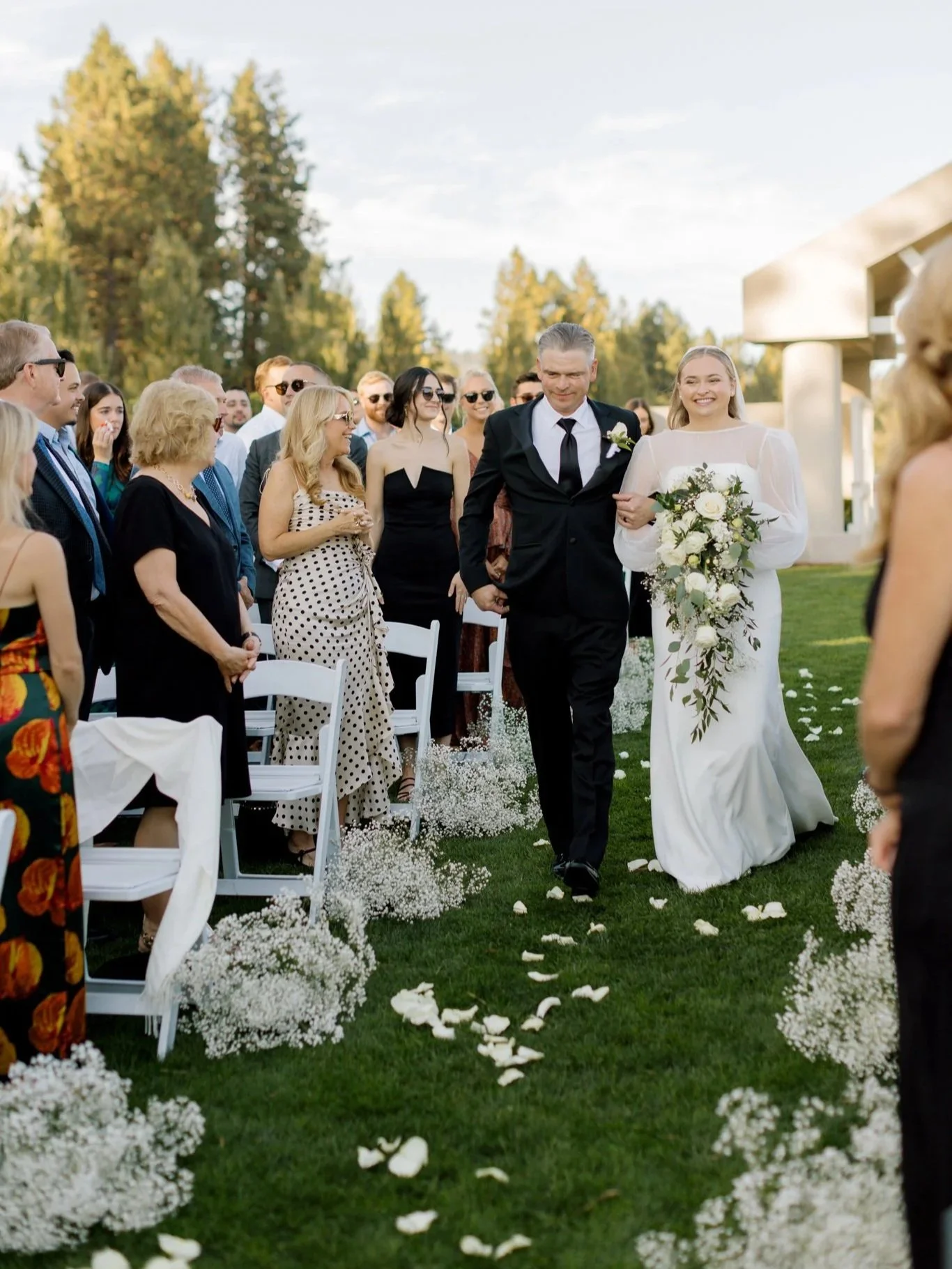 Bride walking down the aisle arm-in-arm with her father, surrounded by guests and floral aisle arrangements at a Coeur d’Alene wedding.