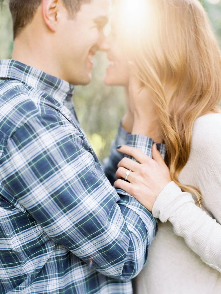 A happy couple close together outdoors, smiling and about to kiss, with sunlight shining on them.