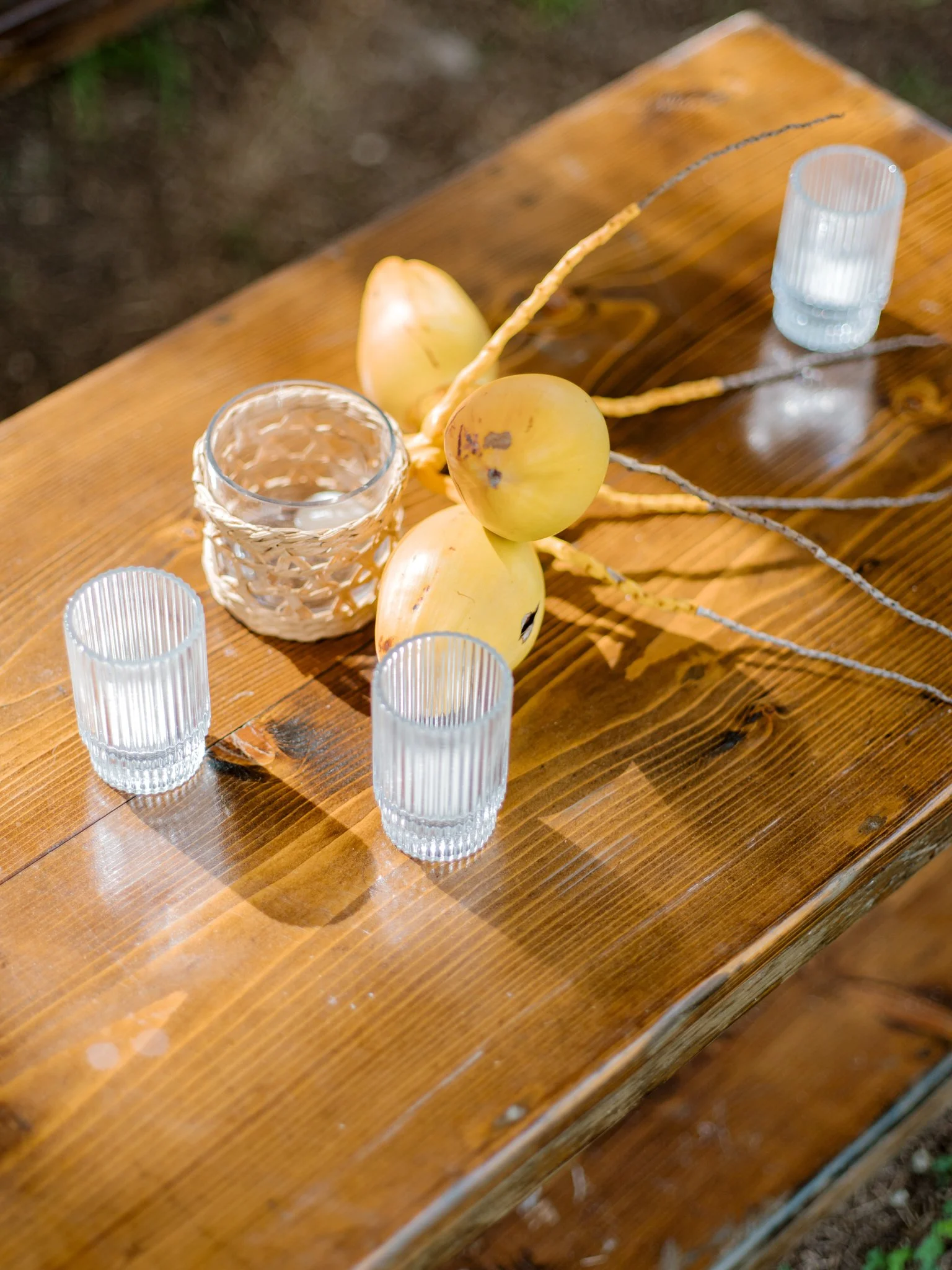 Decorative display with four shot glasses, a glass candle holder, and a bunch of yellow onions with sprouts on a wooden surface.