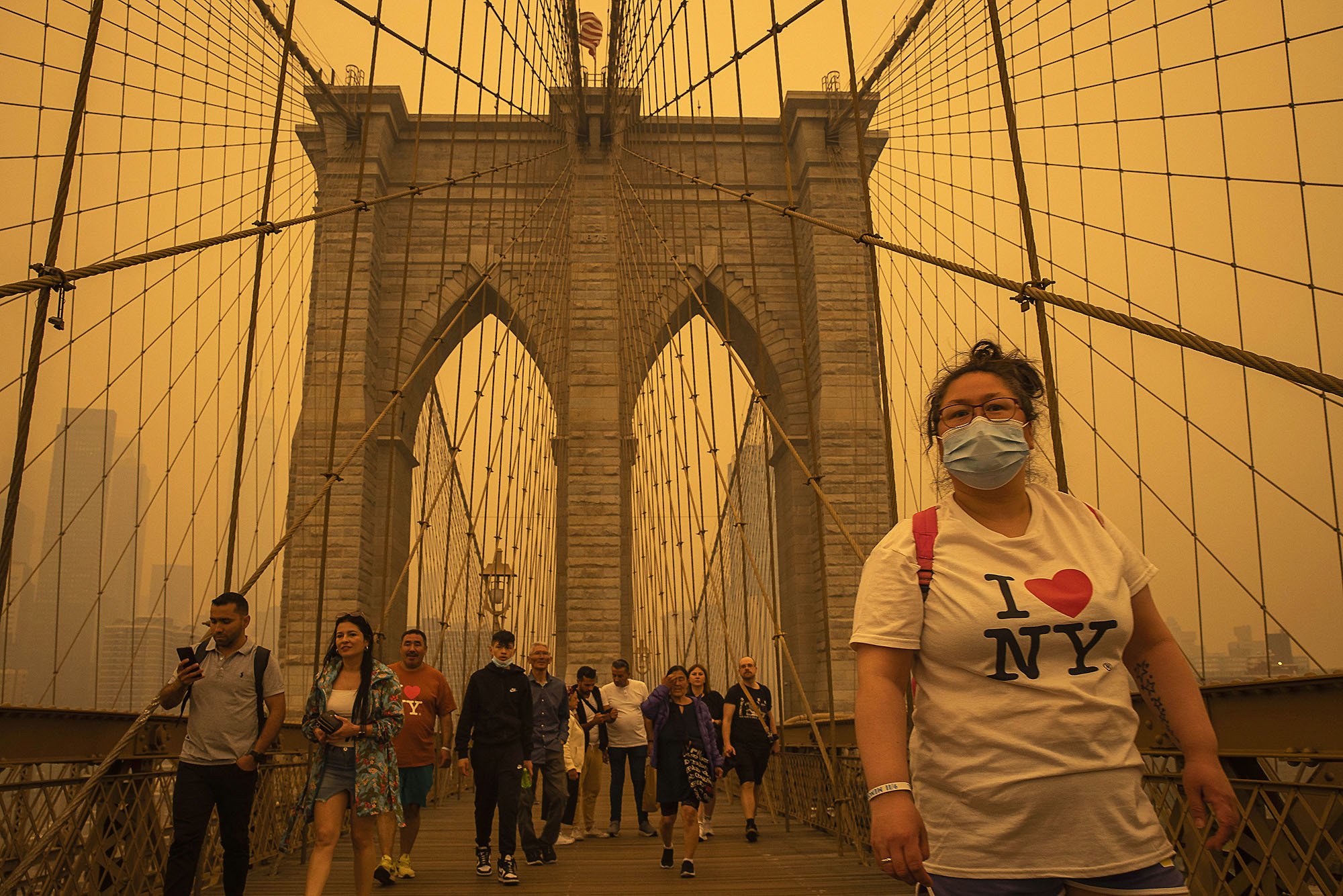  People cross the Brooklyn Bridge through an orange haze as smoke from northern wildfires moves across the city. New York, NY 