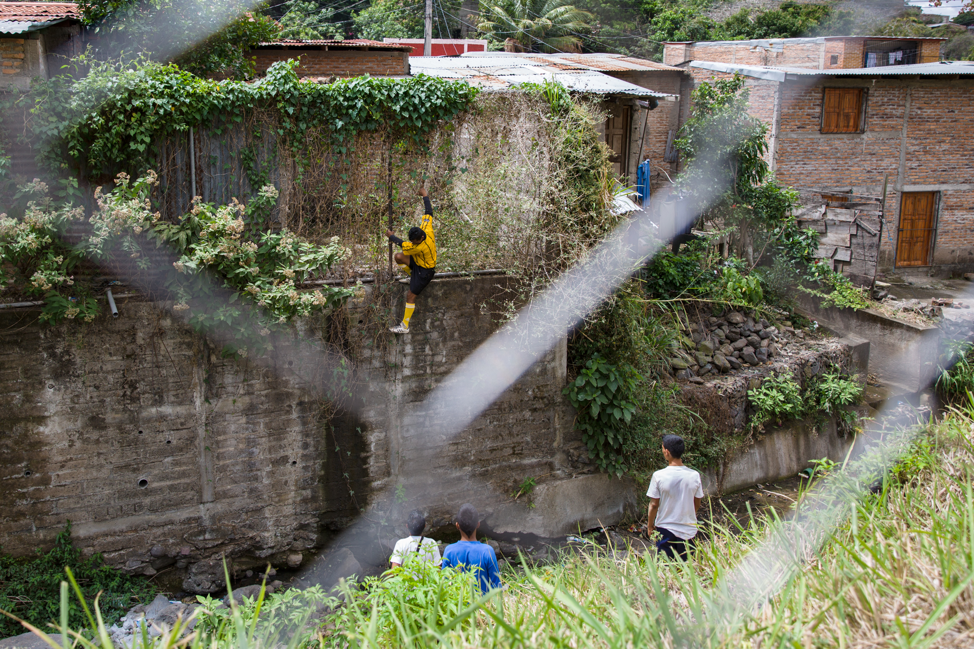  Jairo Blanchard (center) has to retrieve a soccer ball which flies into a neighbor's yard during a match. He climbs down into a ravine and then scales a wall and a fence. Many of the boys line the fence to watch, exclaiming in awe, “Look at him! He’