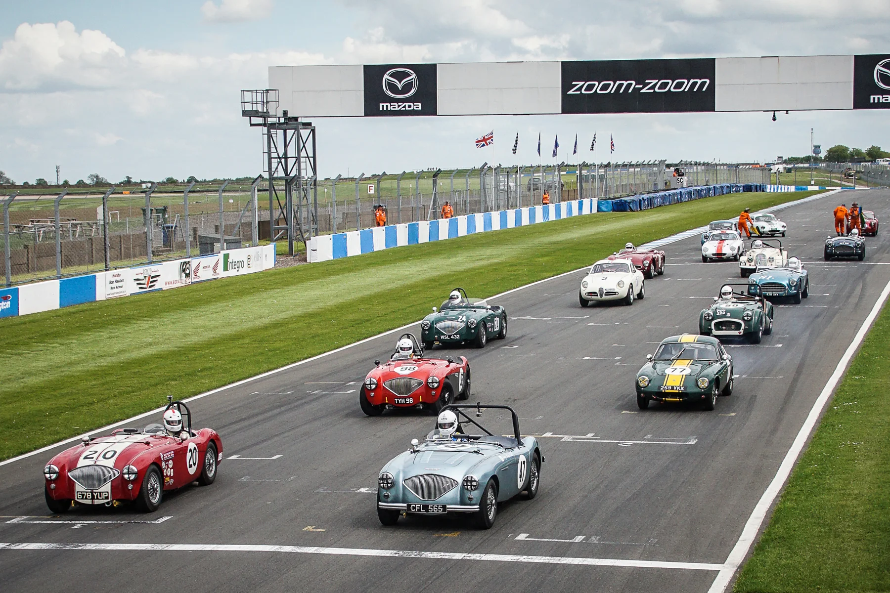 The grid lines up ready for the green flag lap. You will note the absence of Keith Hampson's Sunbeam Alpine Le Mans from the grid and the tell tale smoke emerging from the back of Mike Freeman's Lotus Elite. Story below Photo - Chris Dicken, Tripos Media