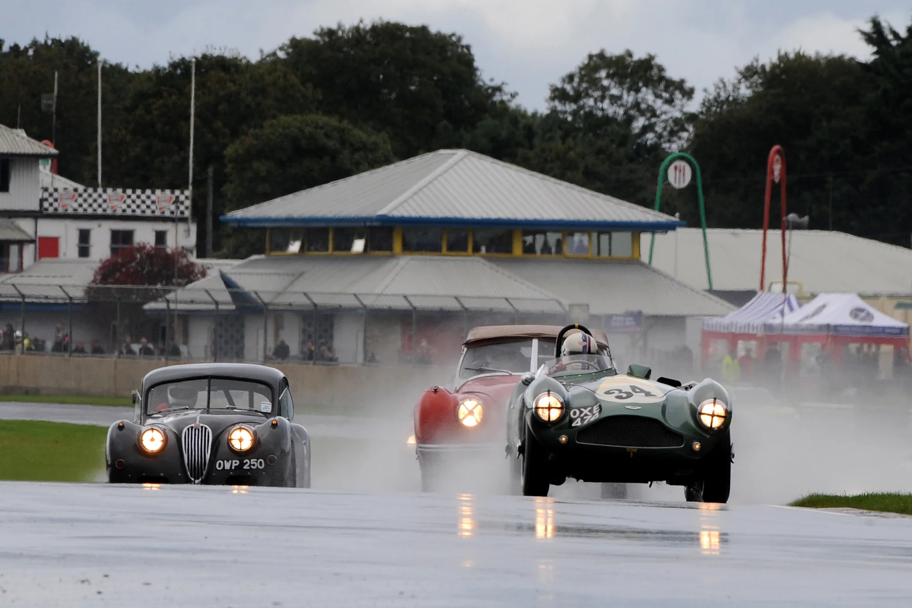 Superb long lens shot taken from Quarry by Jeff Bloxham. Steve Boultbee-Brooks, Geoff Ottley & Kevin Zwolinski, crest Avon Rise for the first time. The distance to the Paddock area behind is forshortened and in fact everyone of the 36 chasing cars are hidden in the spray to the right, behind Kevin's Jaguar. 