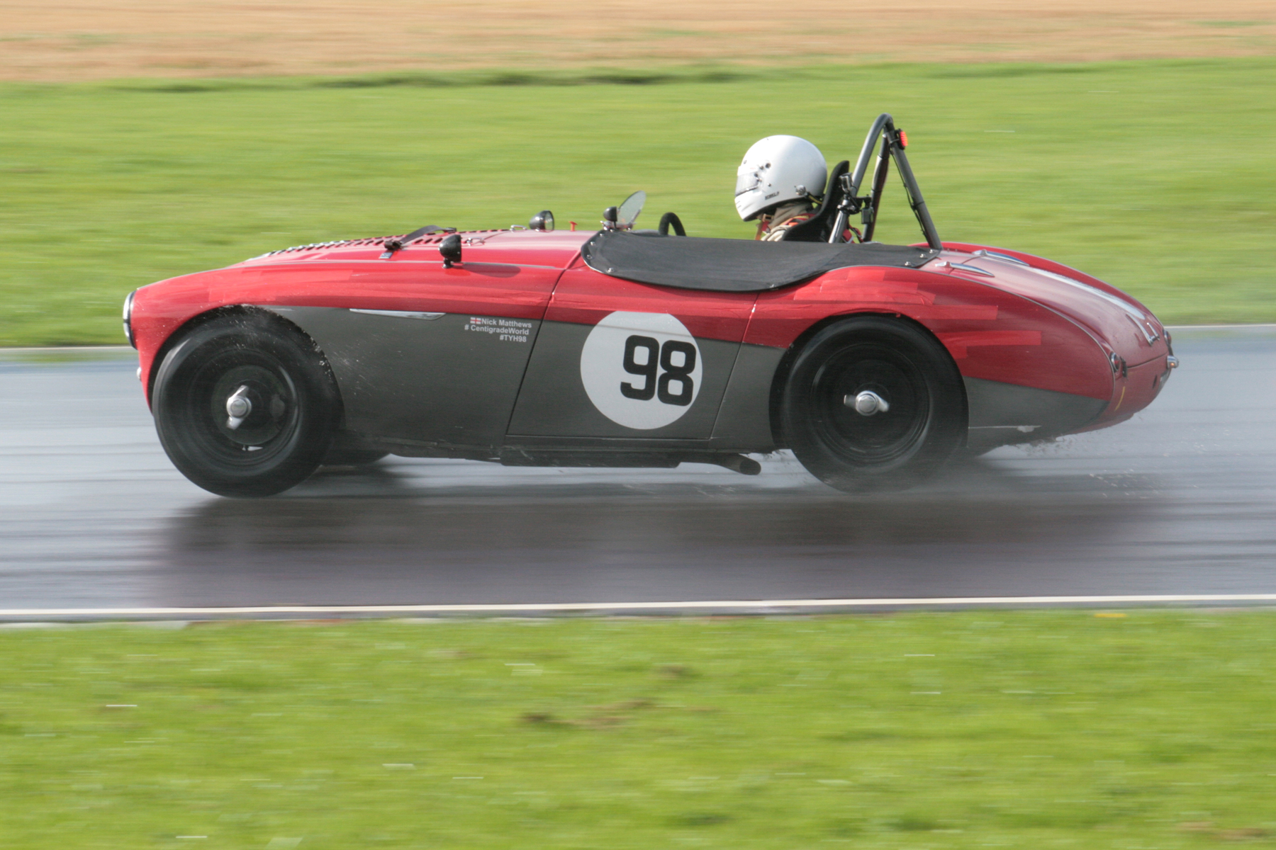 Nick Matthews finished 2nd overall despite his best attempts to avoid the race when during qualifying for the Healey race he overcooked it going into Camp and slid the car along the barriers - fortunately only cosmetic damage ensued - note the strips of red tape along the side. Photo - John Turner
