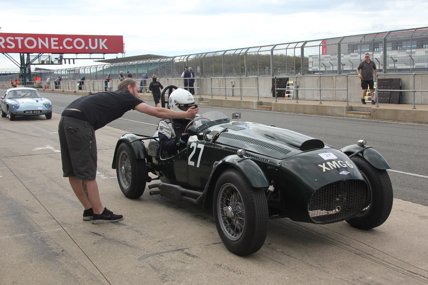 E Williams, having taken the Frazer Nash over from Martyn Corfield, is timed out of his pitbox. Behind is Brian Arculus in the Lotus Elite and on the pitwall, right is Paul Woolmer. Photo - Pat Arculus, Tripos Media