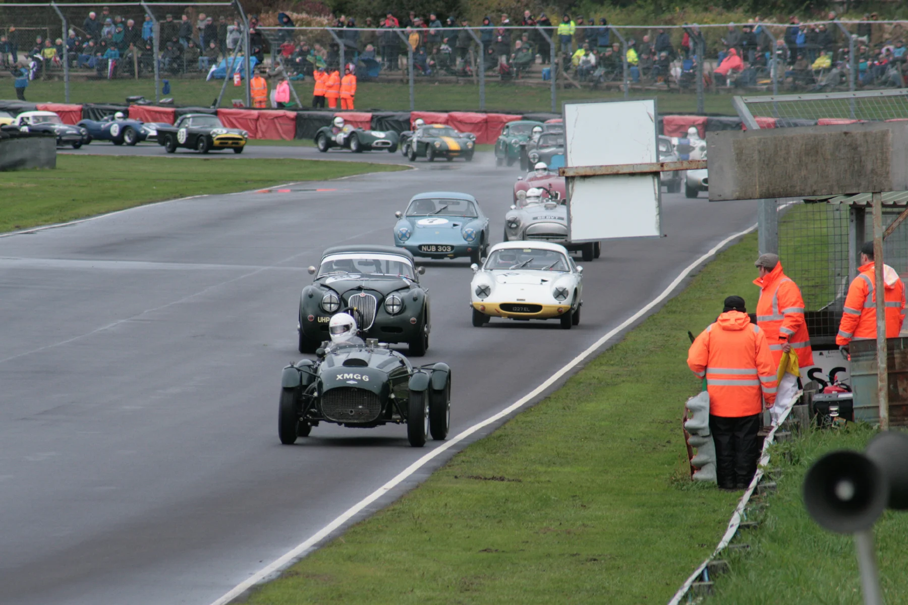 The pack charges through Quarry as a great start sees Martyn Corfield in his Frazer Nash Le Mans Replica lead and heading down Farm Straight and under the marshal’s board towards the Esses for the first time. Marc Gordon (Jaguar XK 150) and Robin Ellis (Lotus Elite) give chase. Photo - John Turner