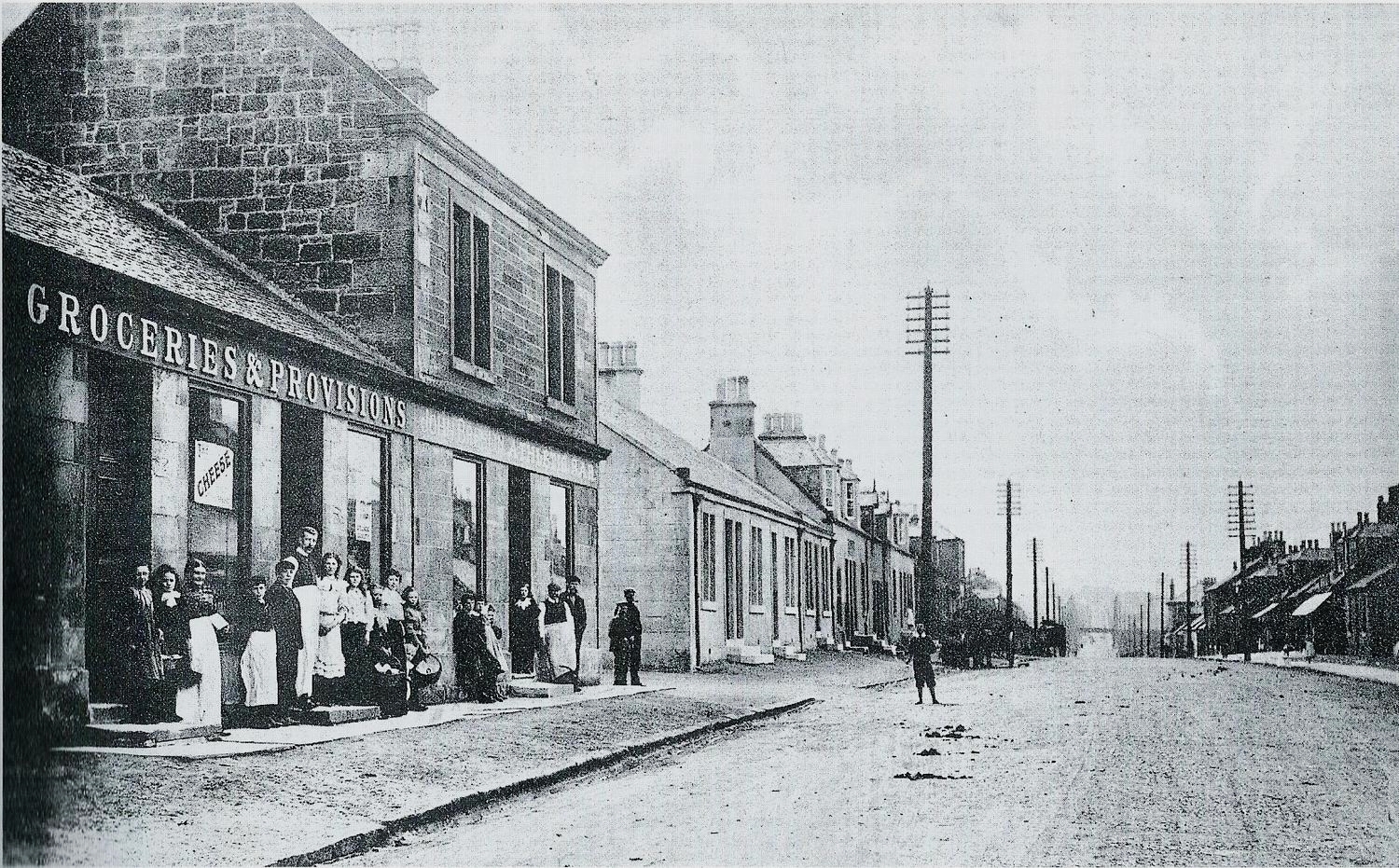 Main Street Harthill White-aproned shop assistants posing for the photo. Little road to left of shops led to the former central bus depot now the funeral parlour. Victoria Street is close by.