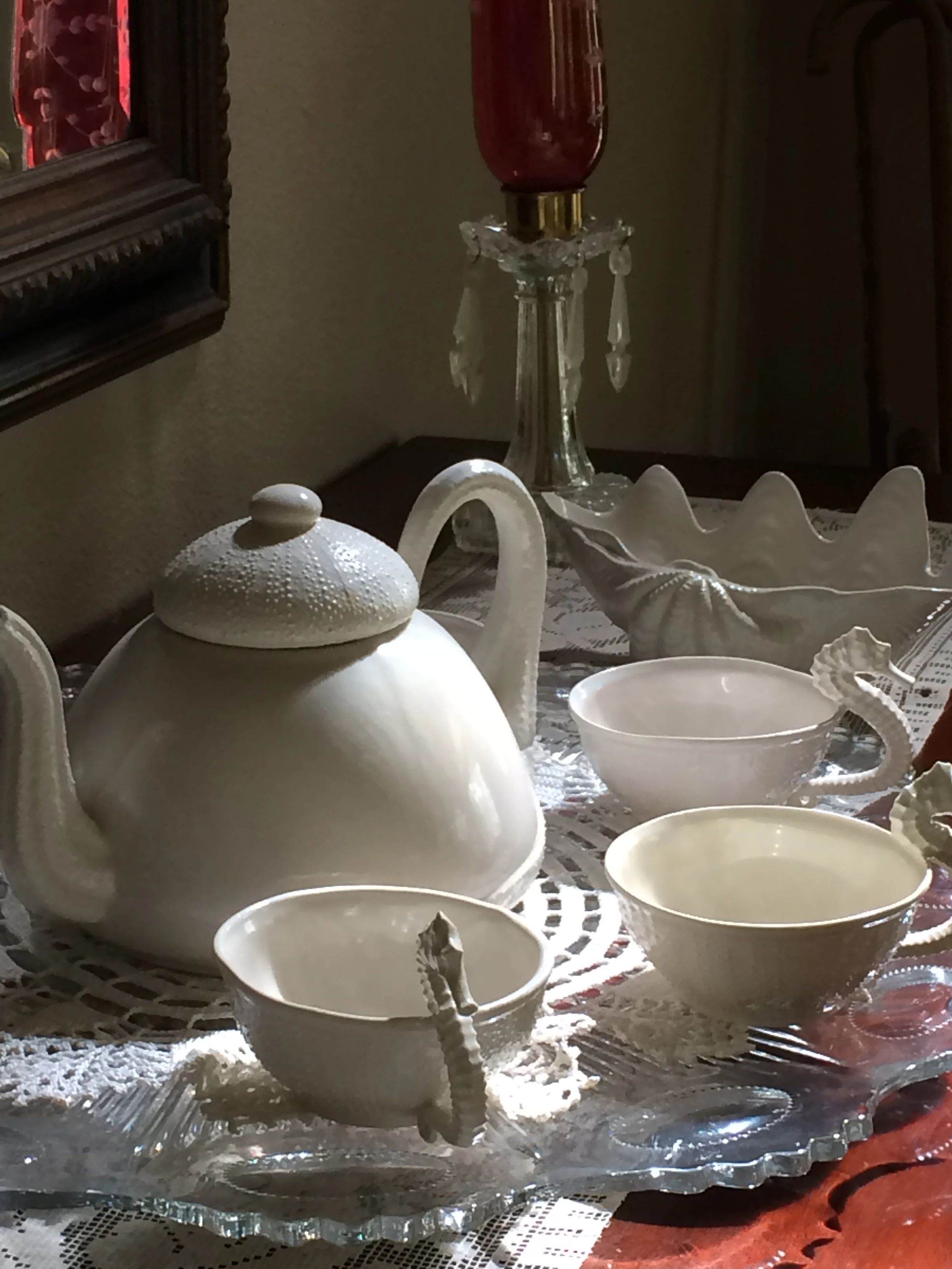 Porcelain Teacups surround a Made in USA Porcelain Teapot in the sunlight