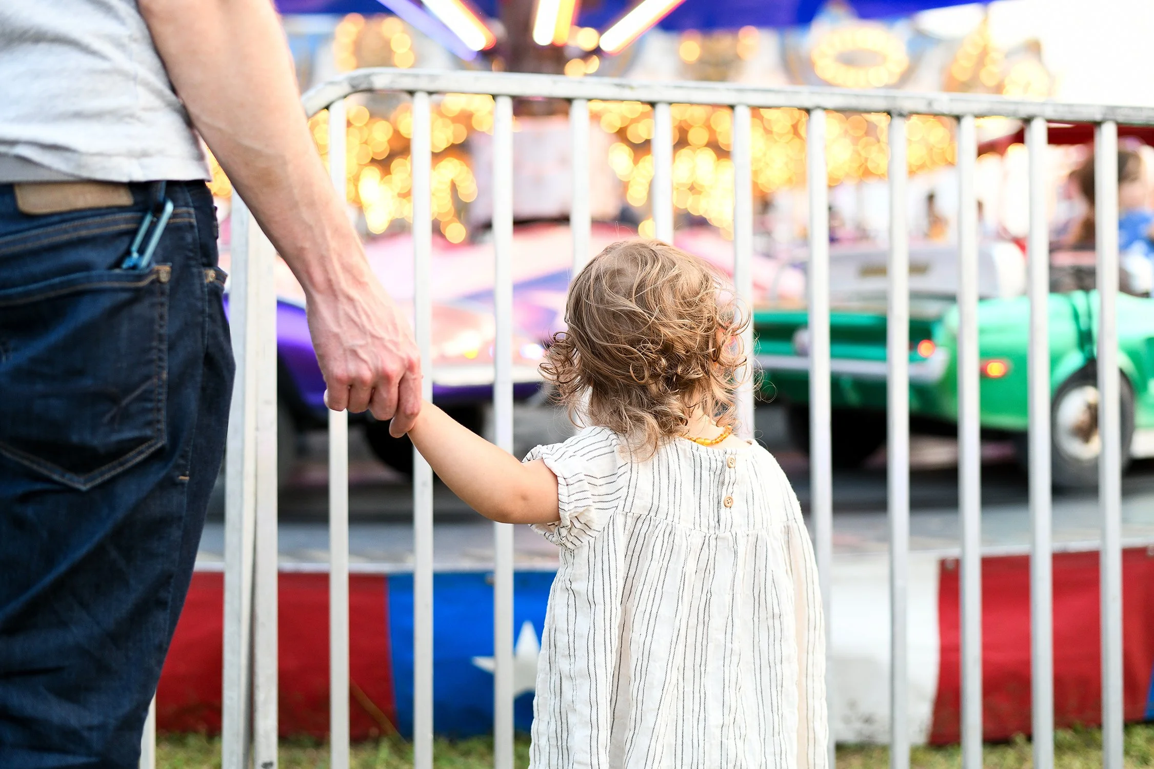 Little Girl holding dad's hand looking at car ride at Monmouth County Fair