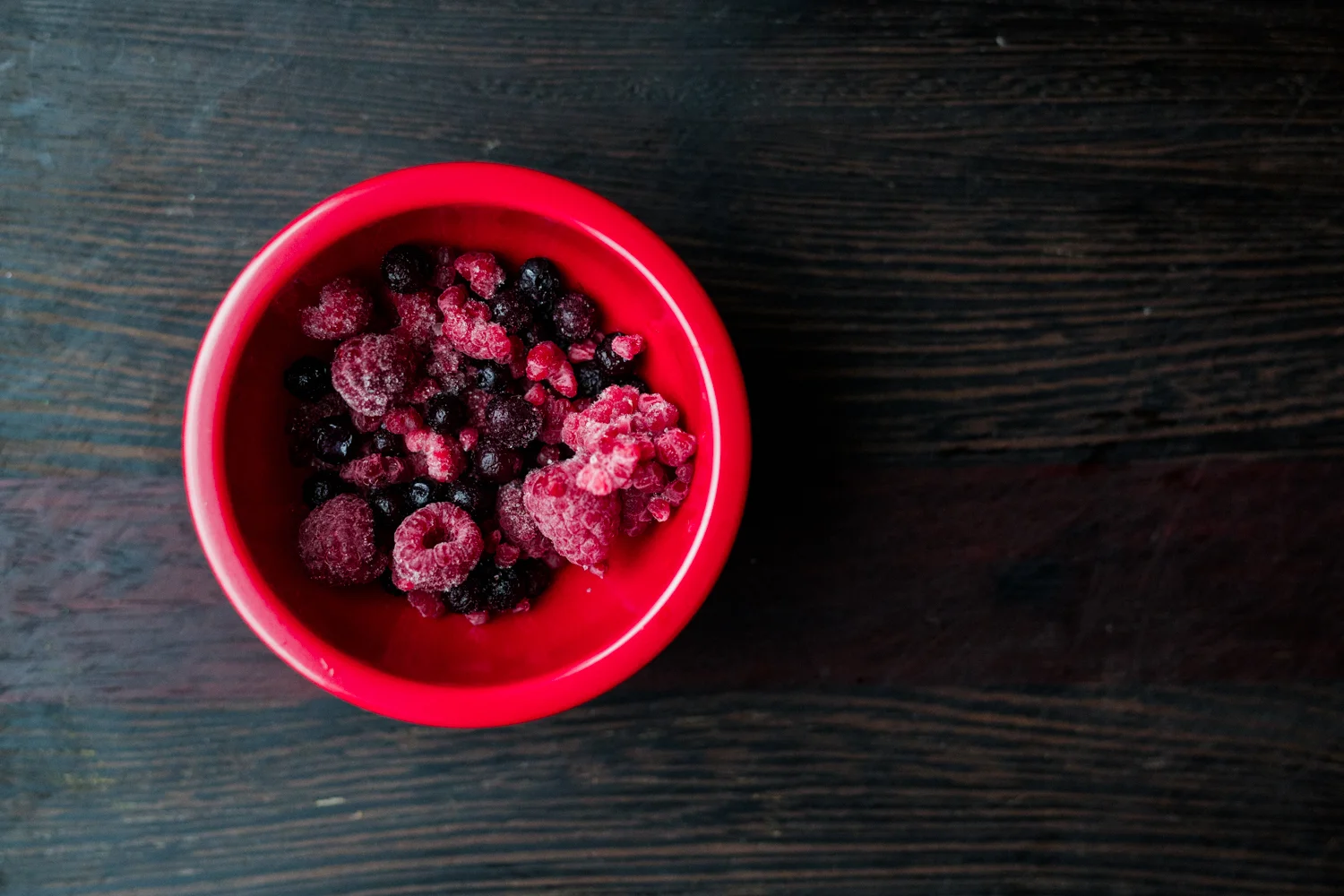 Frozen raspberries and blueberries in a red bowl