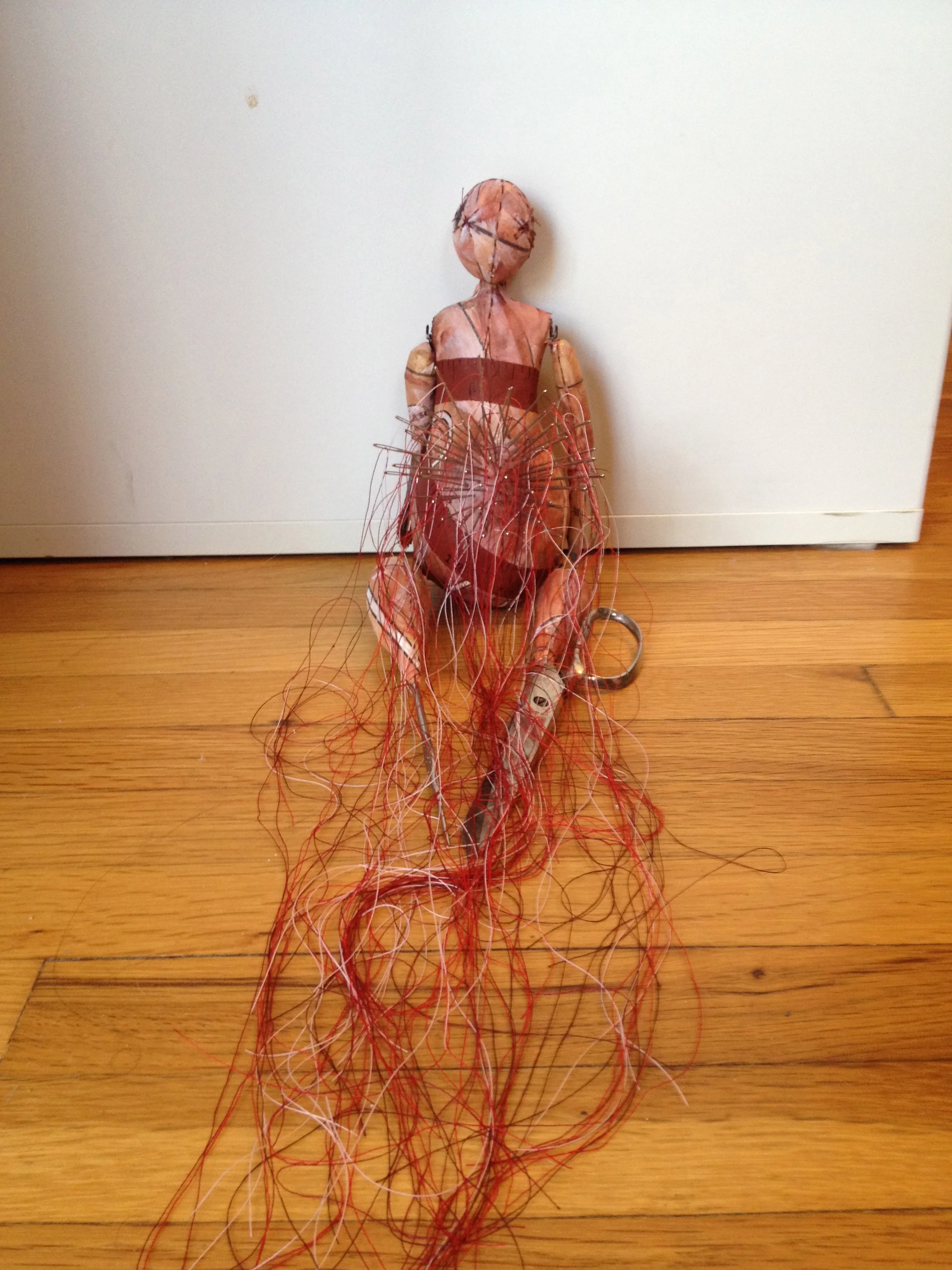 She has different sized sewing needles embedded in the paper clay of her belly. Each of the needles has a portion of thread that hangs beneath her legs. 