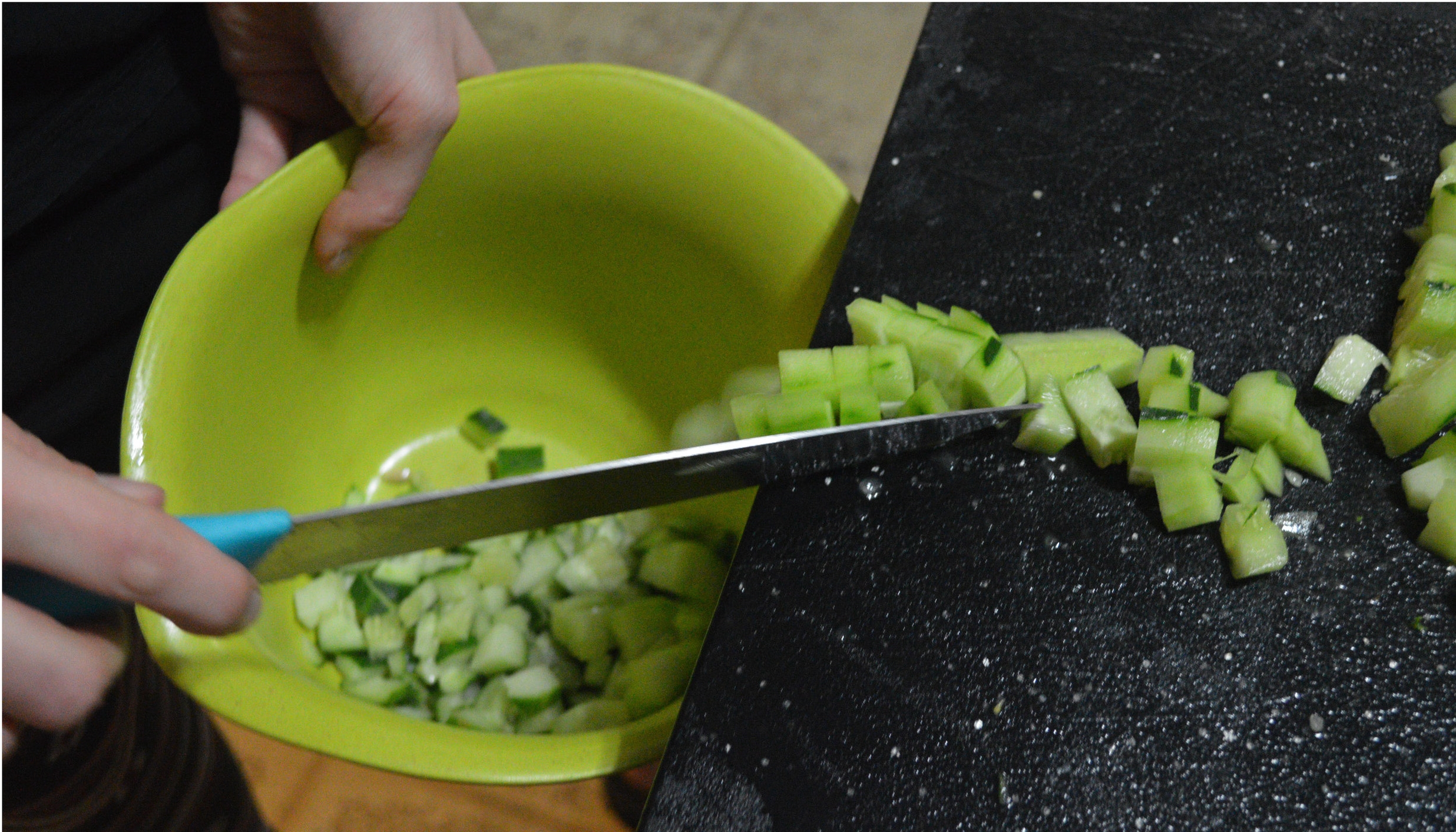 KITCHEN 2: A knife is used to push vegetables into a bowl from a cutting surface.