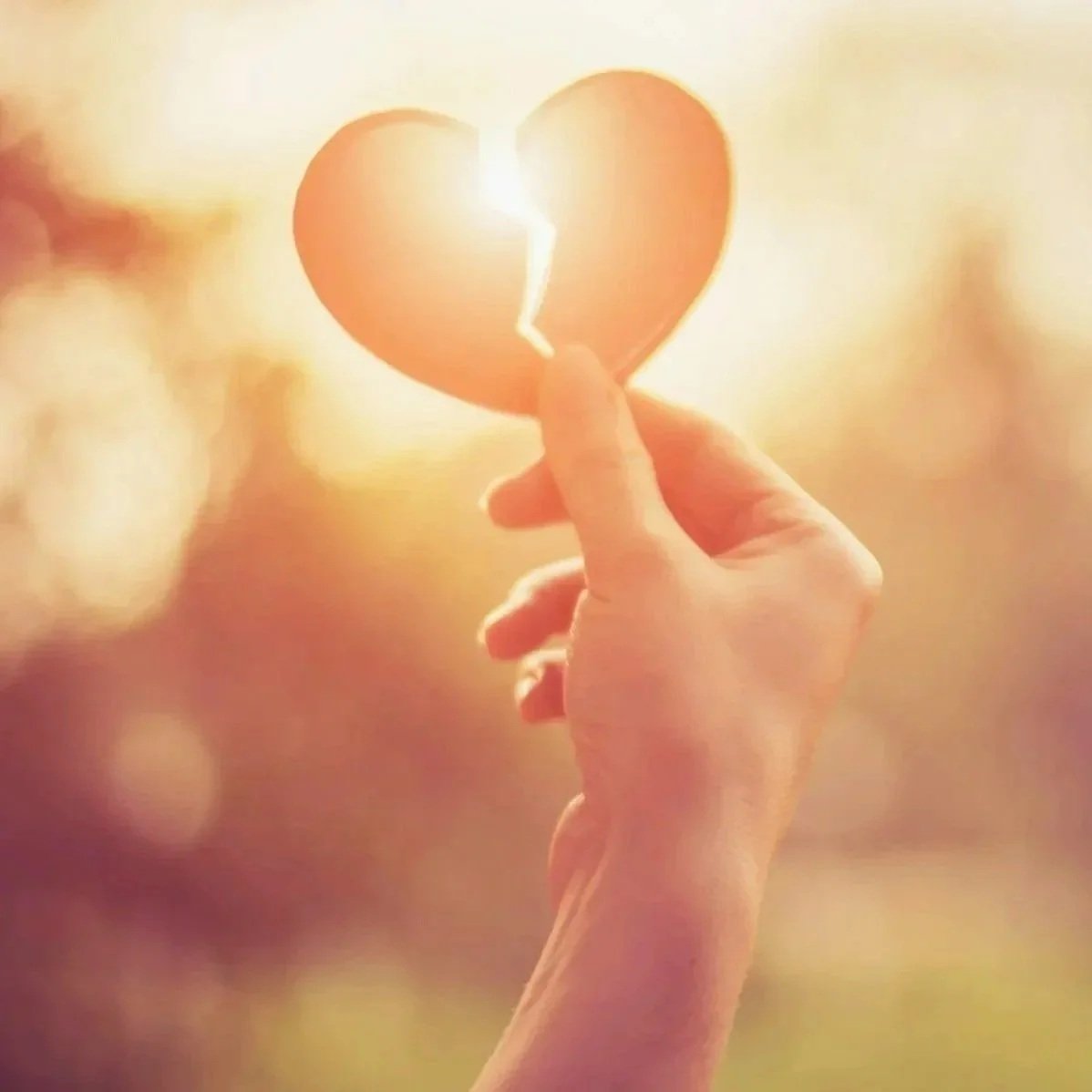 Woman's hand holding a torn paper heart up to the light, a gesture of tenderness toward grief and healing