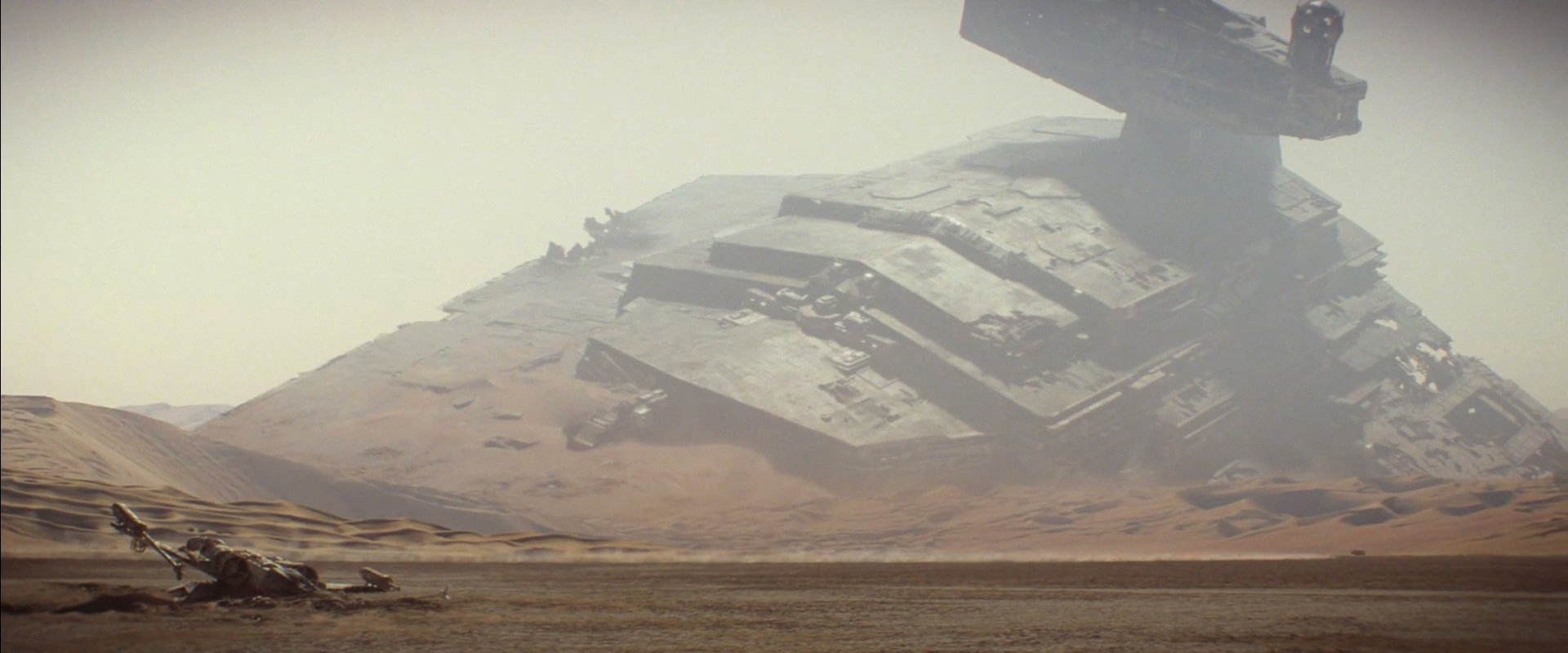 That's no mountain, it's a spaceship. An Imperial Star Destroyer to be exact. In the foreground a downed X-Wing fighter. Both victims of the "Battle of Jakku" which we will see in the upcoming game Star Wars: Battlefront (BTW - New trailer ). The X-Wing is one from the classic trilogy as the split wings engine is a full circle.