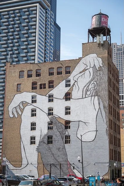 A photo of a mural painted on a building in Chicago, showing a man sitting with eyes closed, a hand on his forehead.