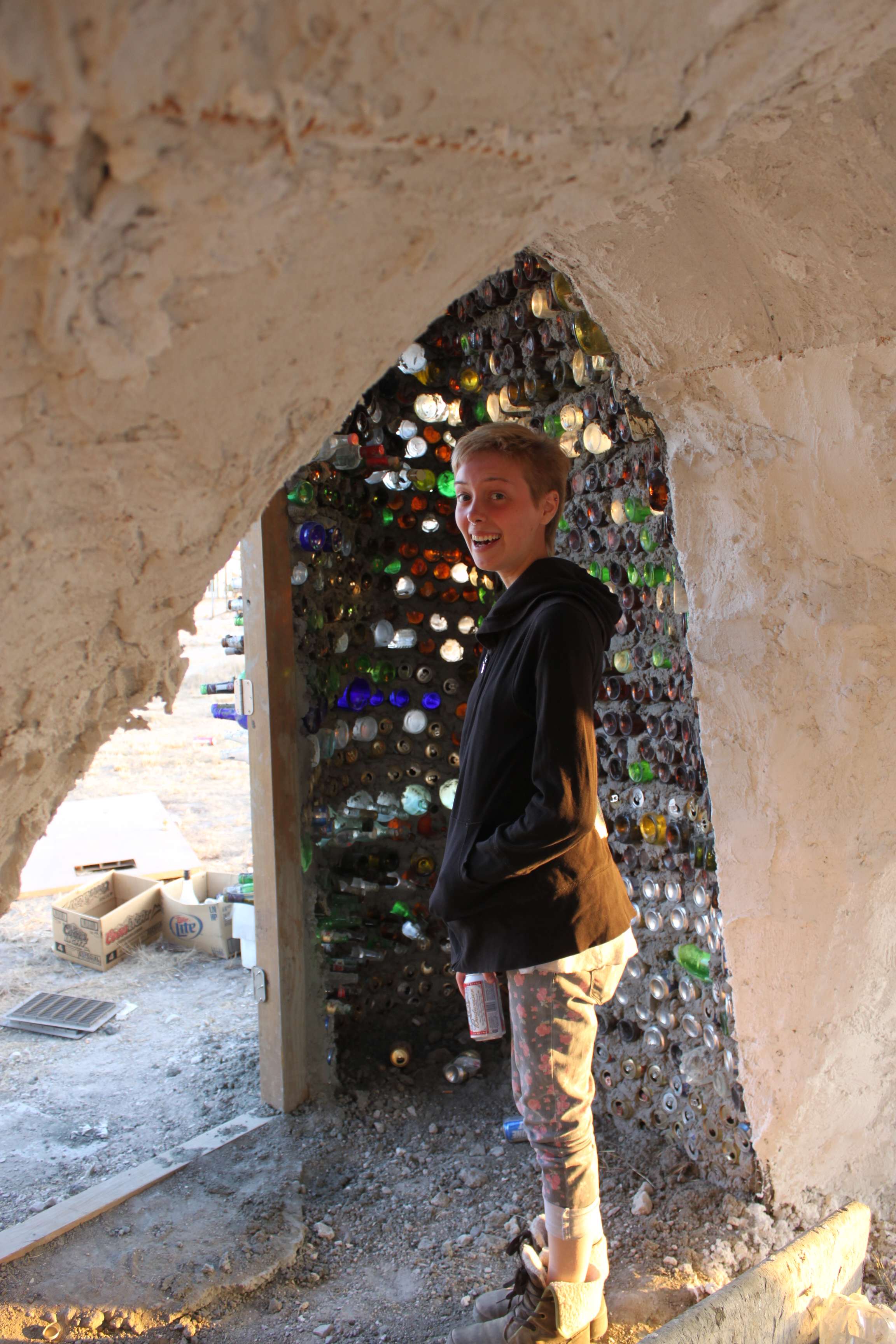 Angie in a castle of old beer cans and bottles. 