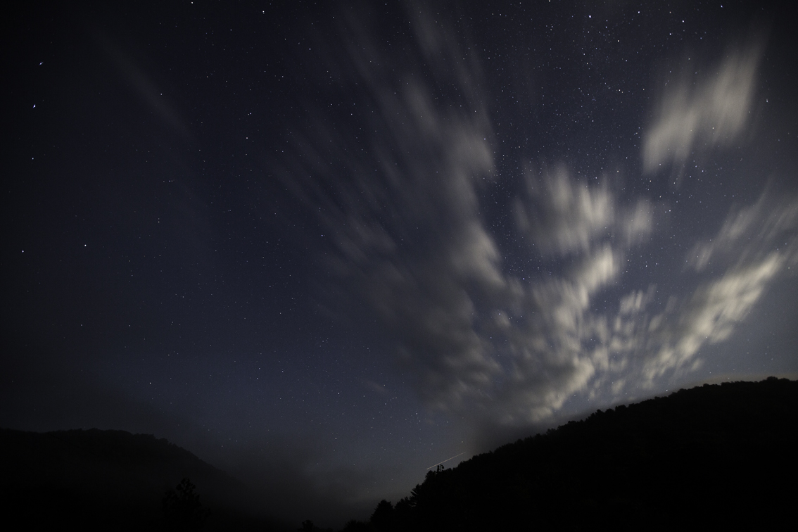 fog rolling into the valley as clouds, lit by the moon, move quickly in