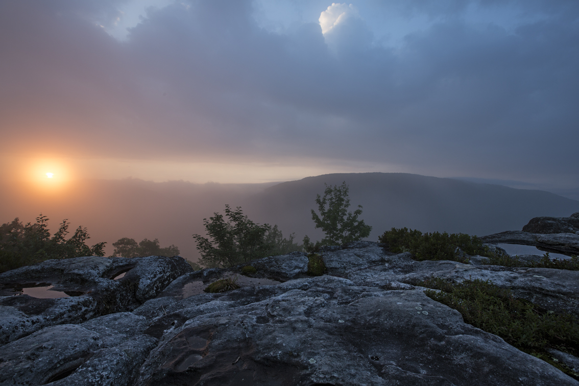 The sun peaking over the mountains, while fog rolls through the valley.