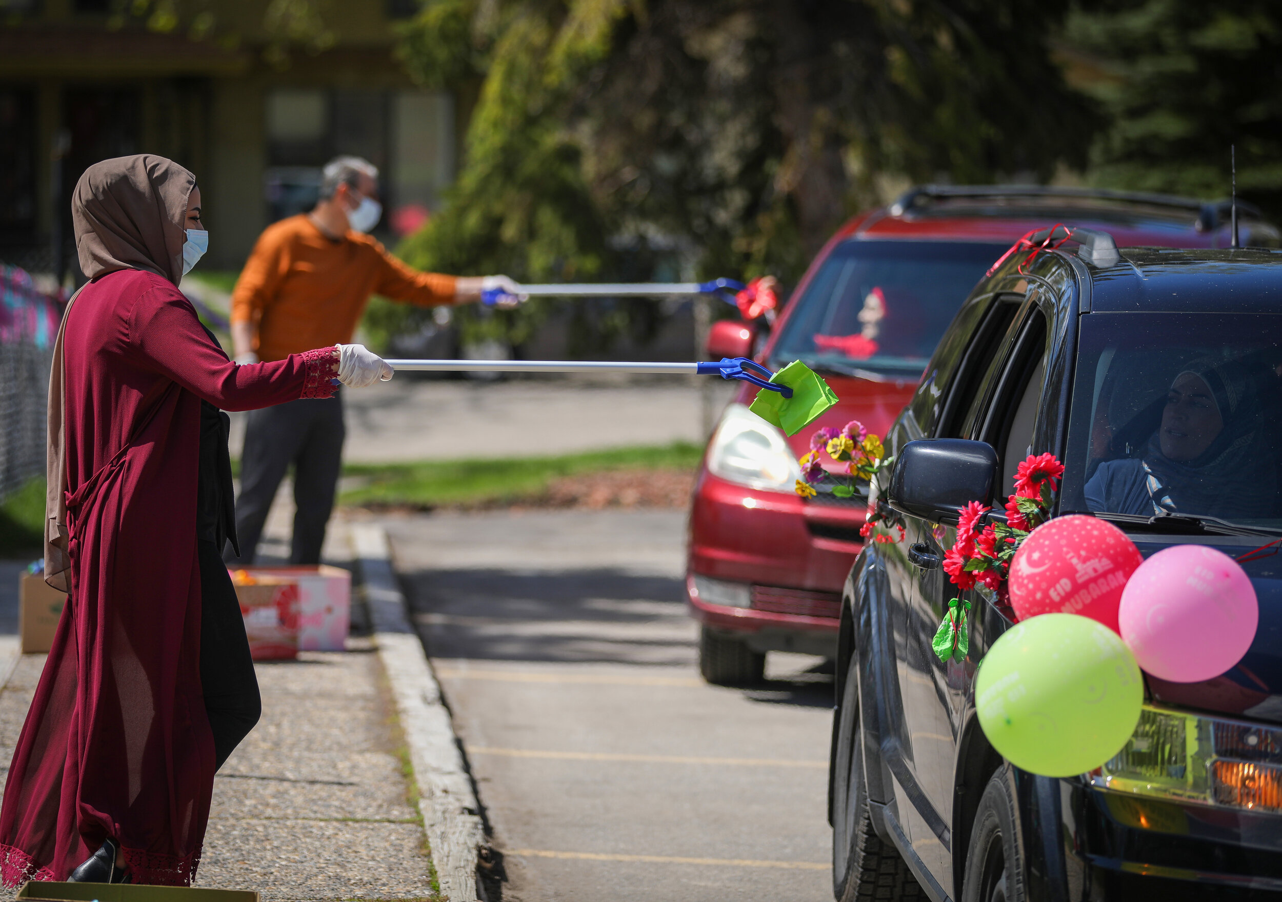  Rana Omar, left, hands out bags filled with treats to children during the drive by Eid at Al-Salam Centre in Calgary on May 24, 2020. 