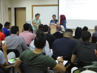 Professor Lisa, Dr. Summer, and a student translator stand before the very packed room of students.