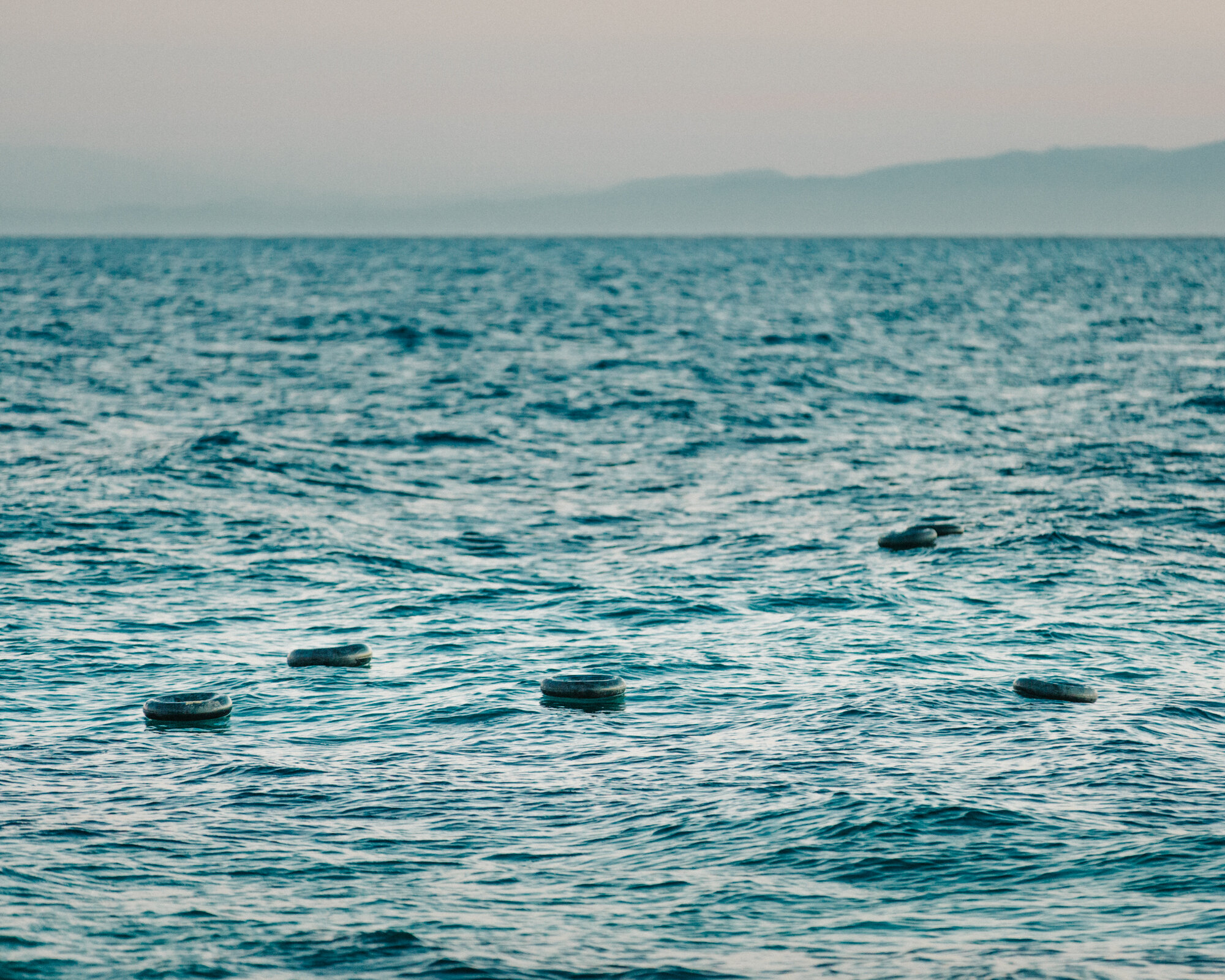  Tire inner tubes dot the waters off the coast of Lesvos with Turkey looming in the distance. The tubes serve as makeshift floatation devices for those who cannot afford proper life preservers, which are often subject to extreme price gouging. These 