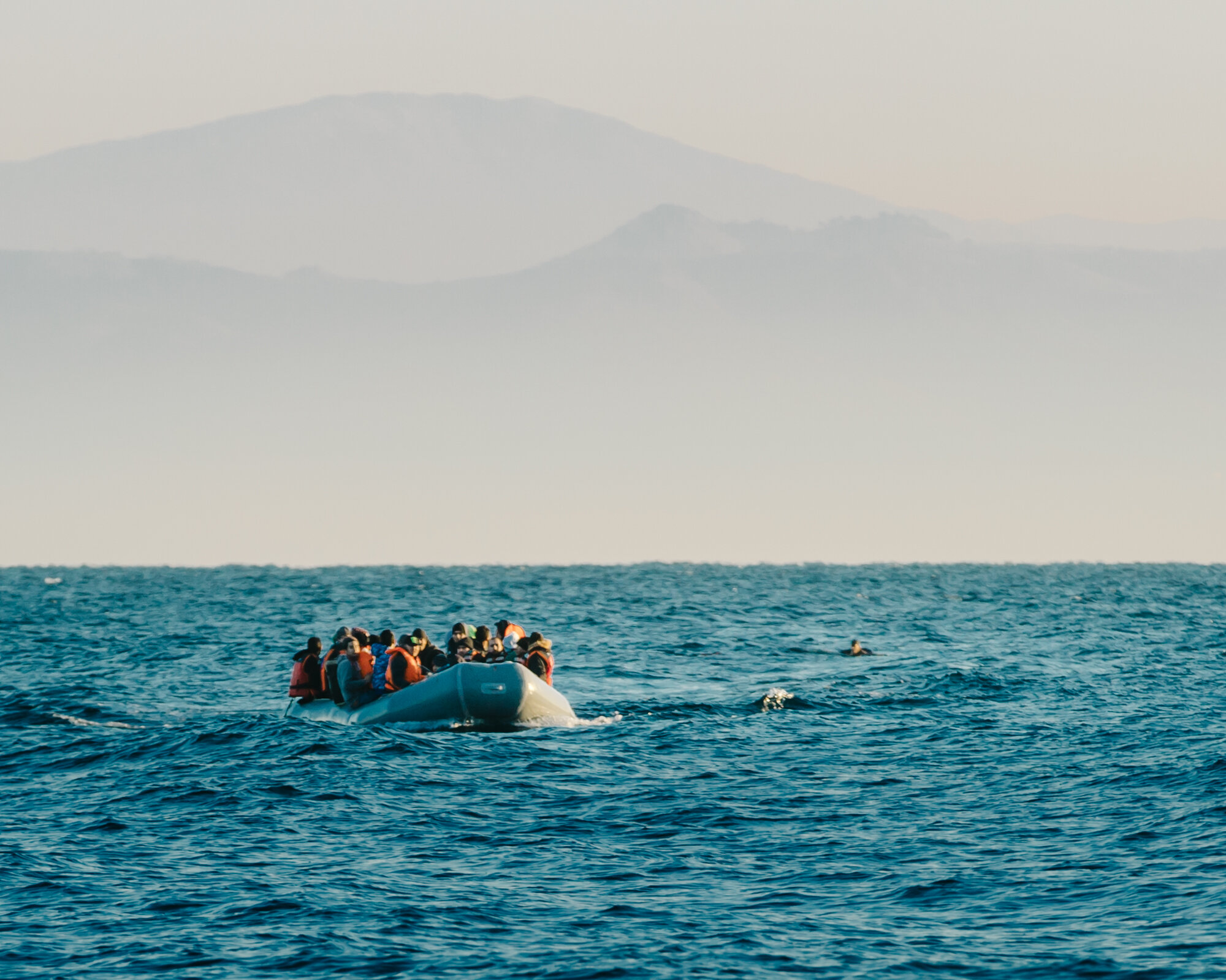  In a moment of panic, a man miscalculated the distance to shore and leapt from the raft despite protests from the others. To the right of the dinghy, he struggles to stay afloat in the offshore current. 