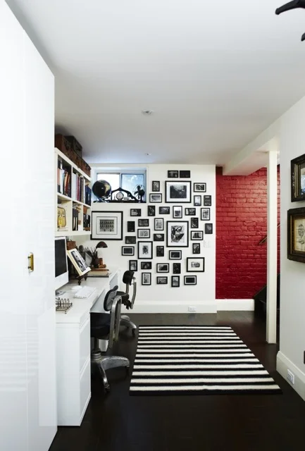 A painted red brick wall adds some colour to the black and white home office. A wall of picture frames and a striped area rug creates a sense of character in the space. (Casey Design / Planning Group Inc. - photograph by Angus Fergusson)