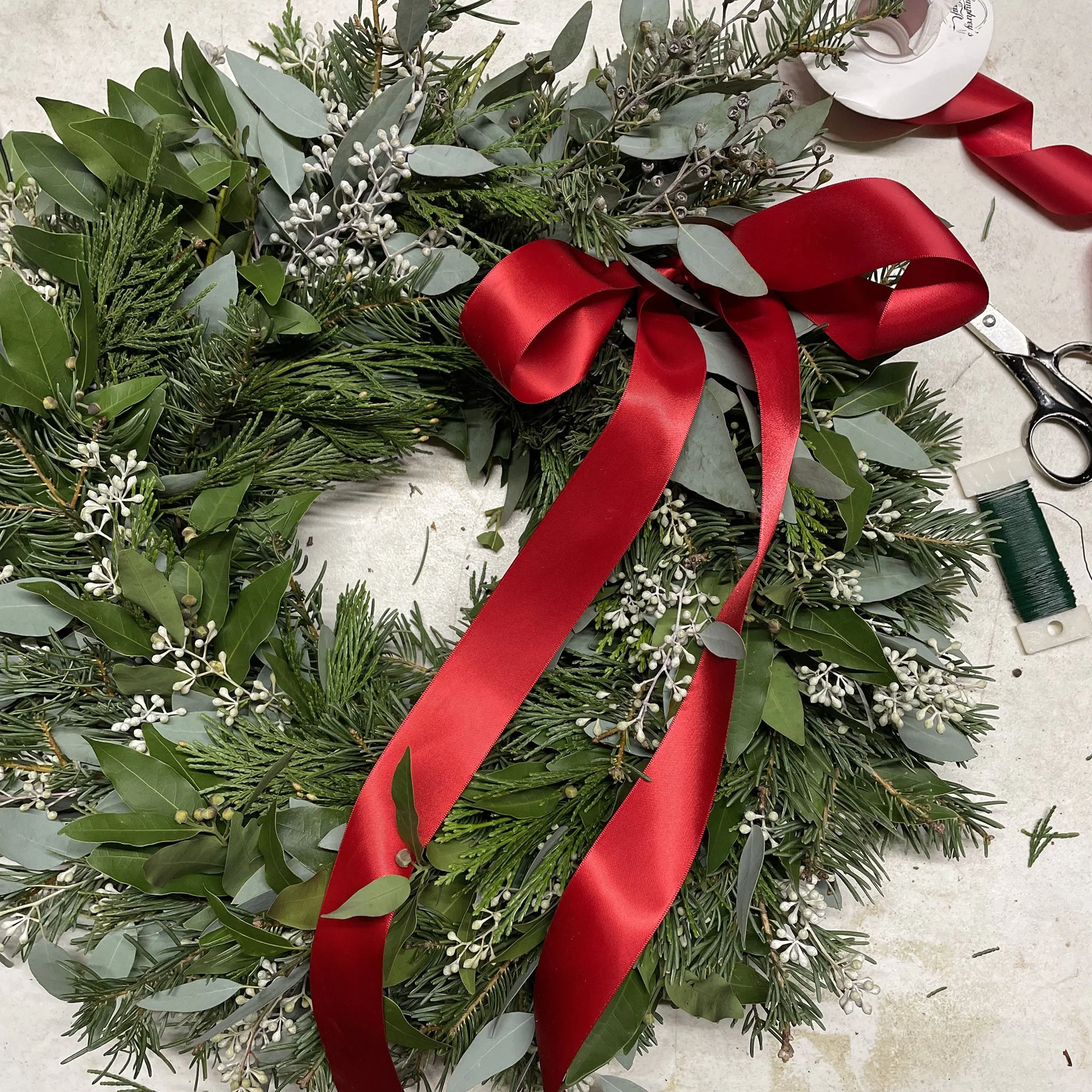 A photo of a lush wreath with a red ribbon and crafting supplies.
