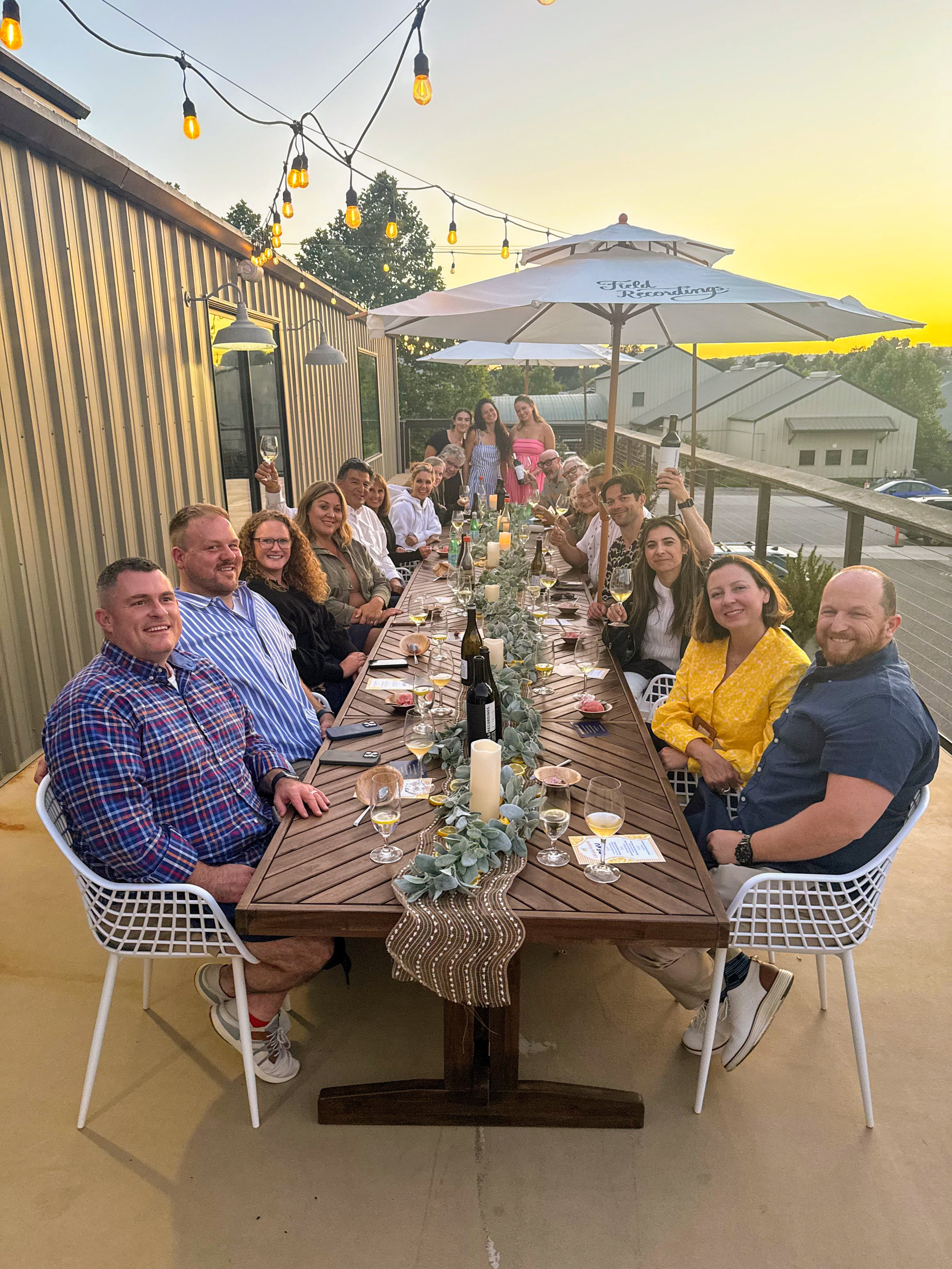 A group of people sit around a long wooden table, decorated with a lush centerpiece.