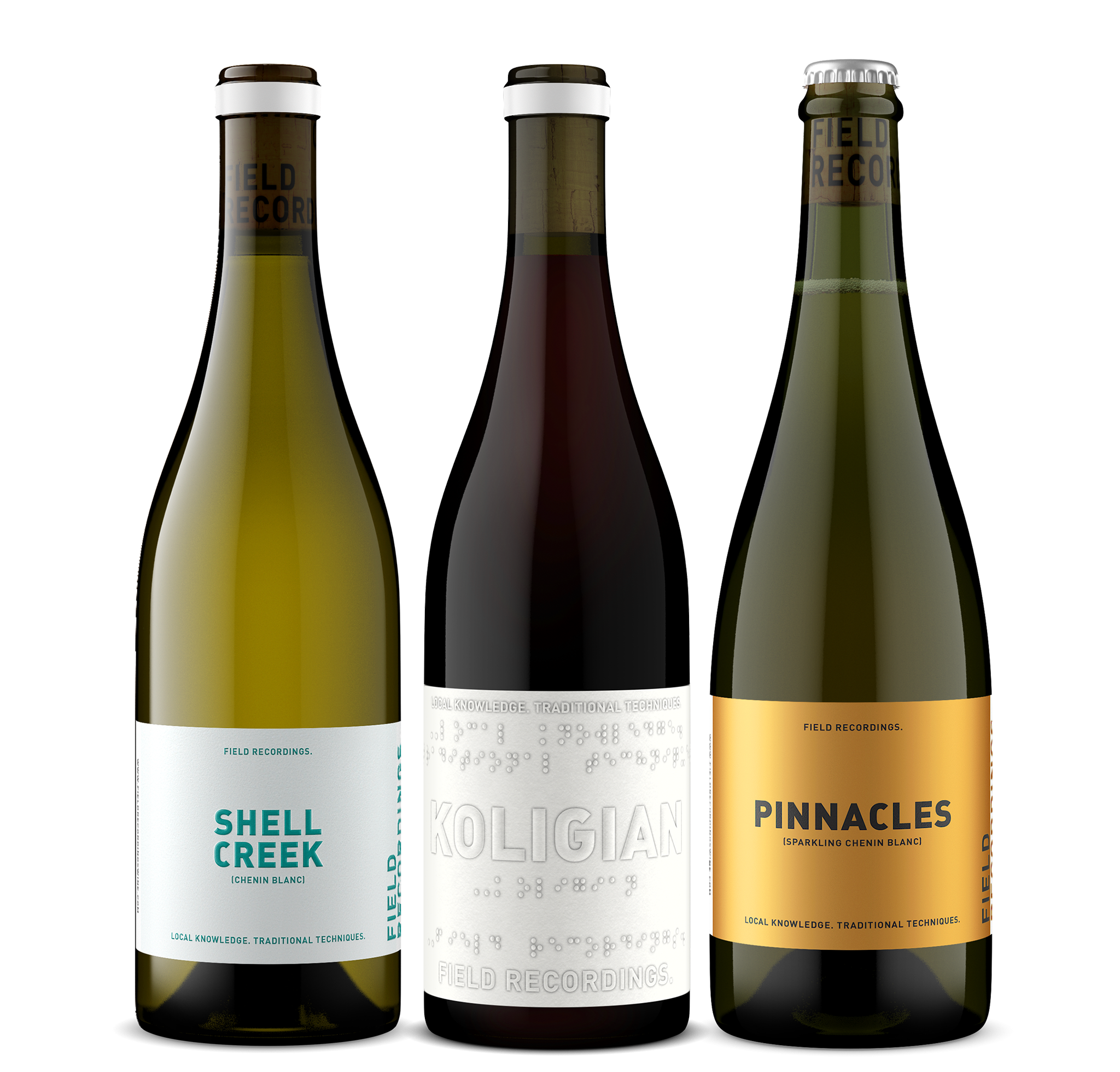 Three bottles of wine arranged in a row. From left to right: Jurassic Park Chenin, green glass with a blue label; Koligian red field blend, with black glass and a white label; Pinnacles sparkling Chenin Blanc, with green glass and a gold label.