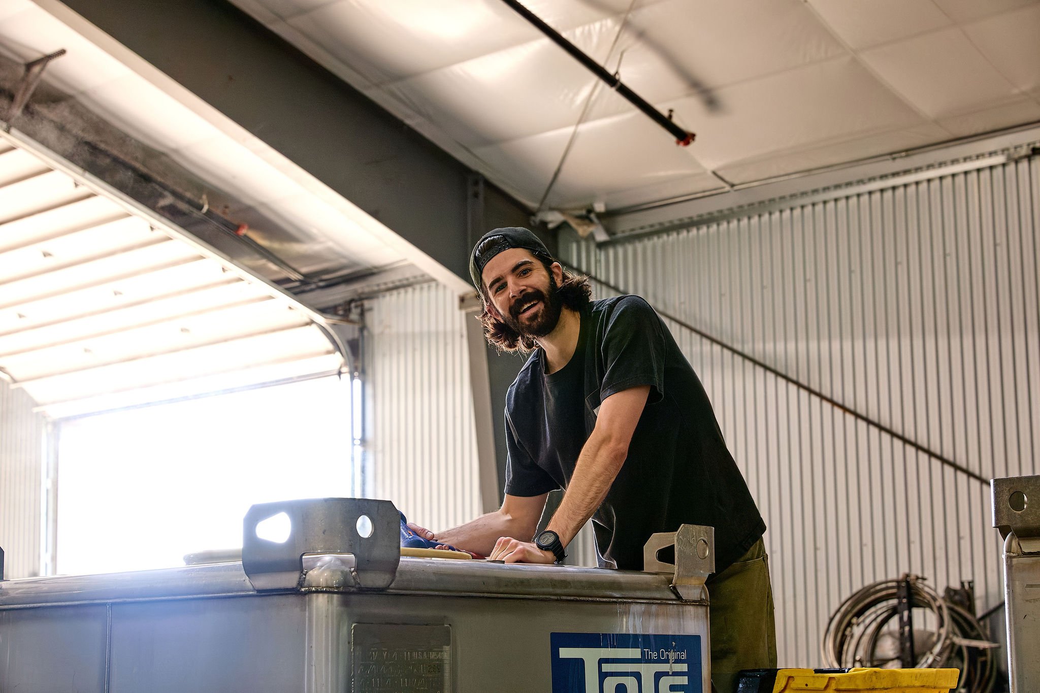 A person smikes as they rinse out a stainless steel tank.