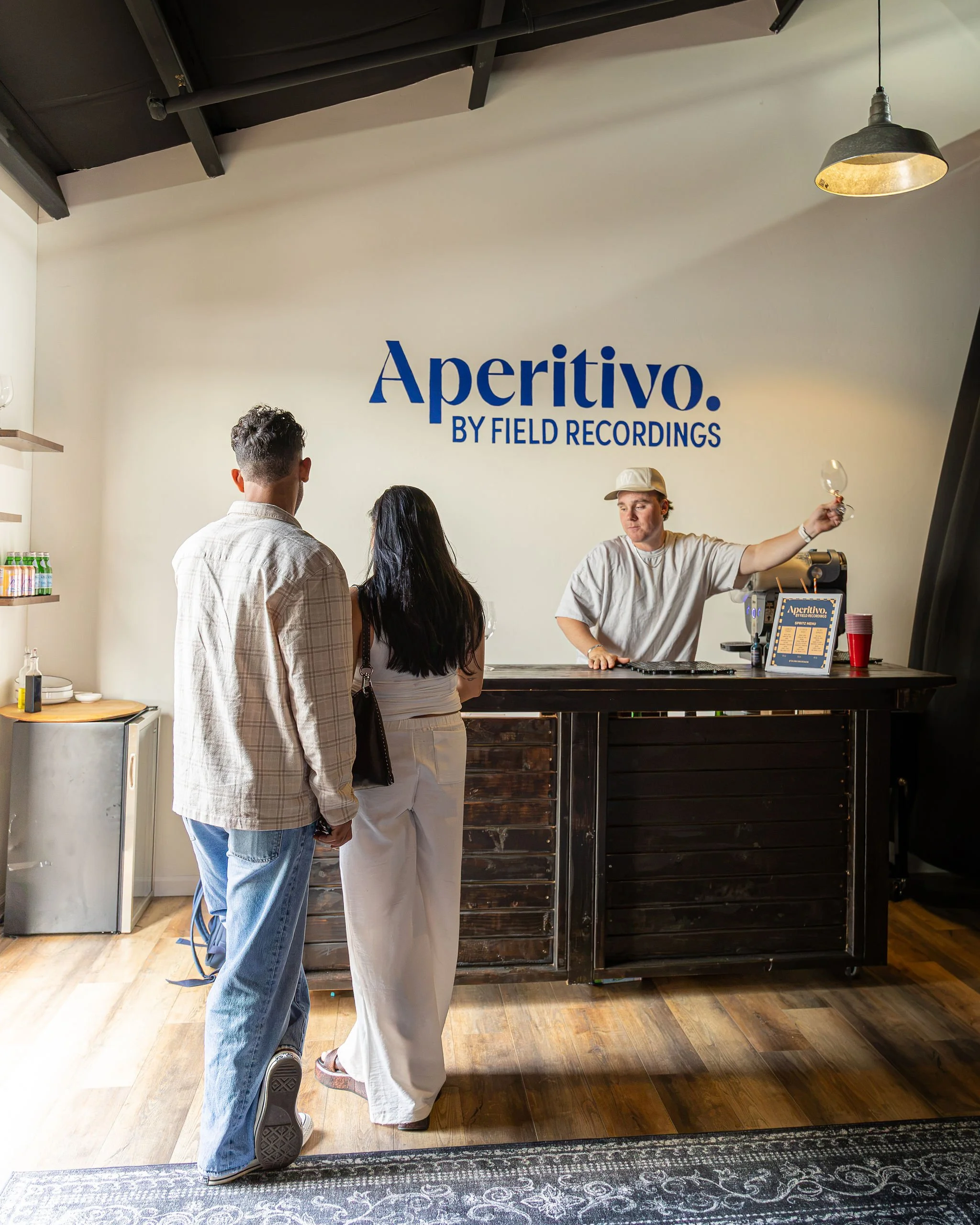 Jack pours a wine at the Aperitivo Bar, while two peole stand and wait.