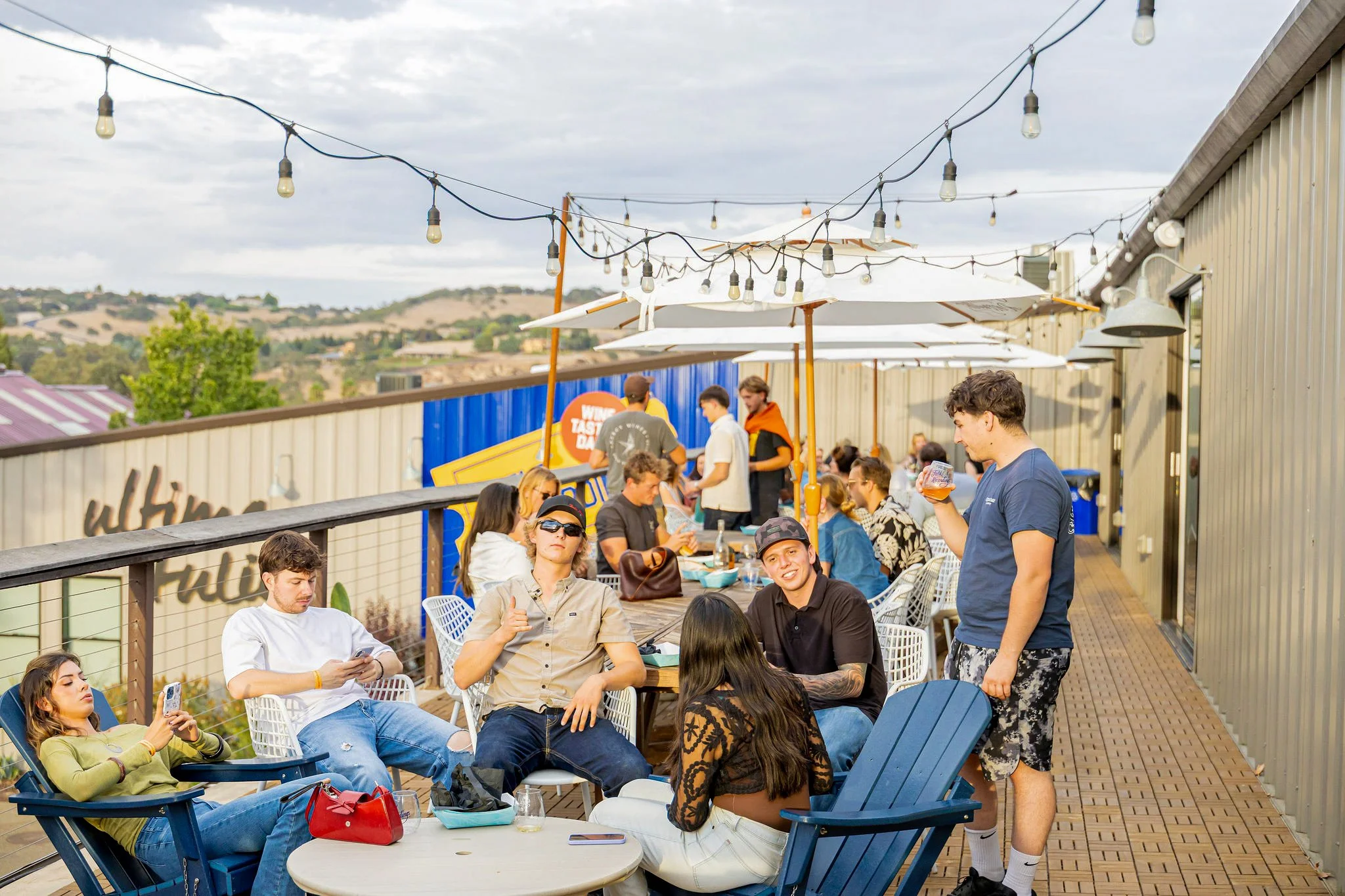 People sit around a patio, with string lights and adirondack chairs.