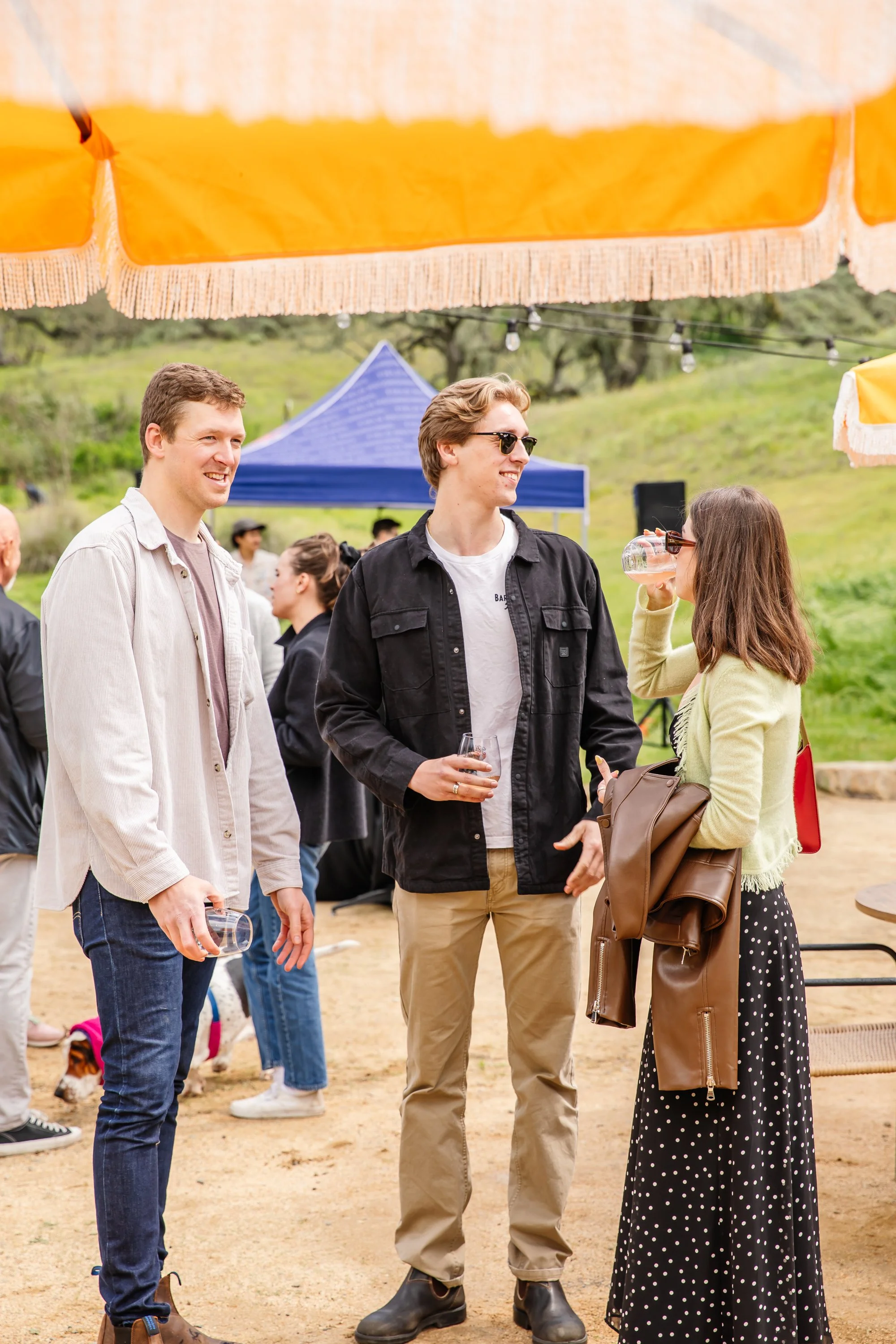 Three people stand and chat while drinking wine at an outdoor patio.