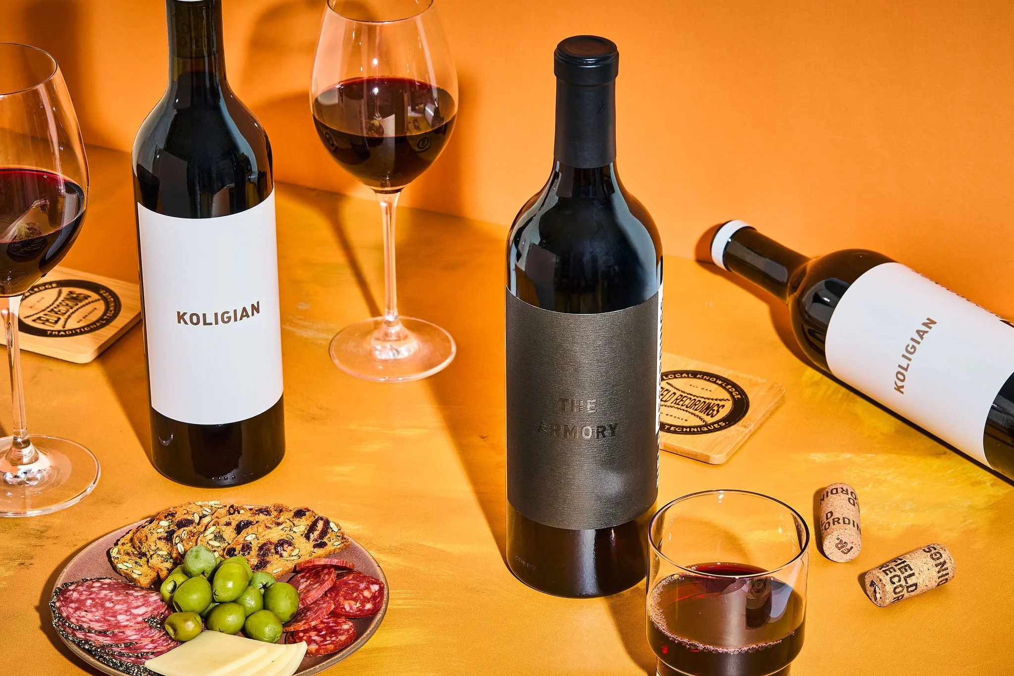 Orange wood table setting with two bottles of wine, a glass of red wine, and a snack plate.