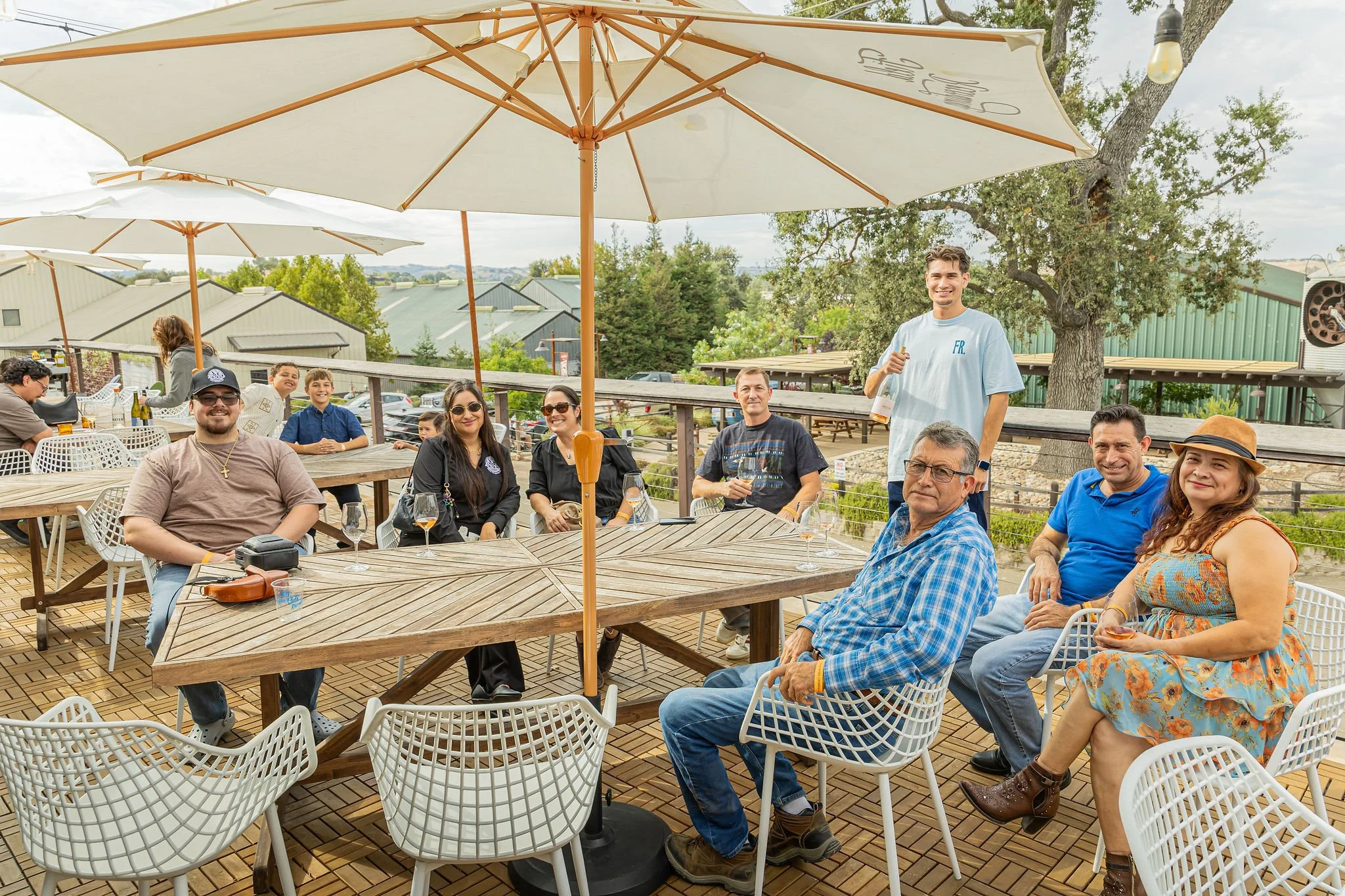 A group of people smile as they sit on a patio overlooking trees and tin city.
