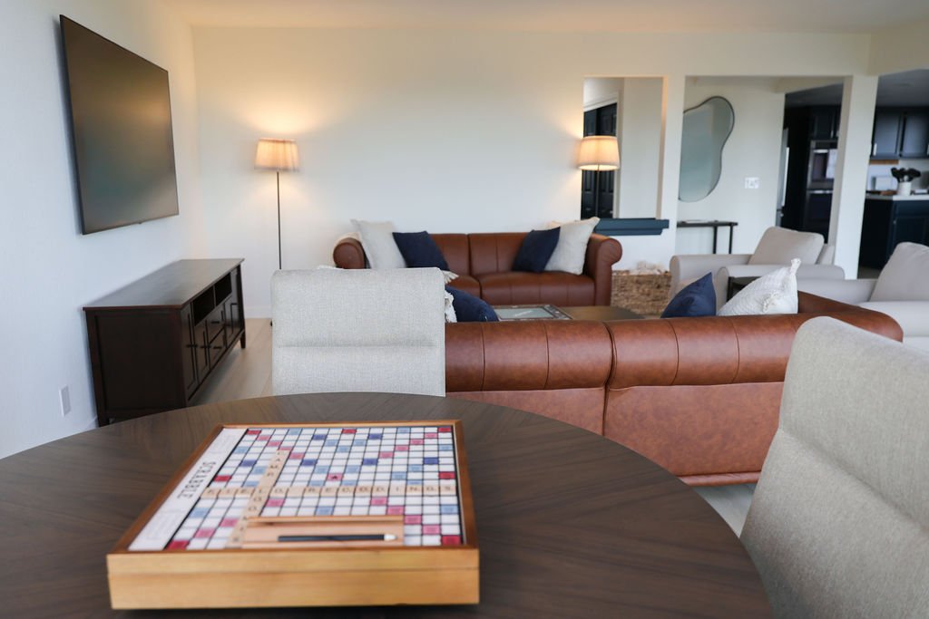 Living room with leather sofas, armchairs, a wall-mounted TV, and a game board on the dining table.