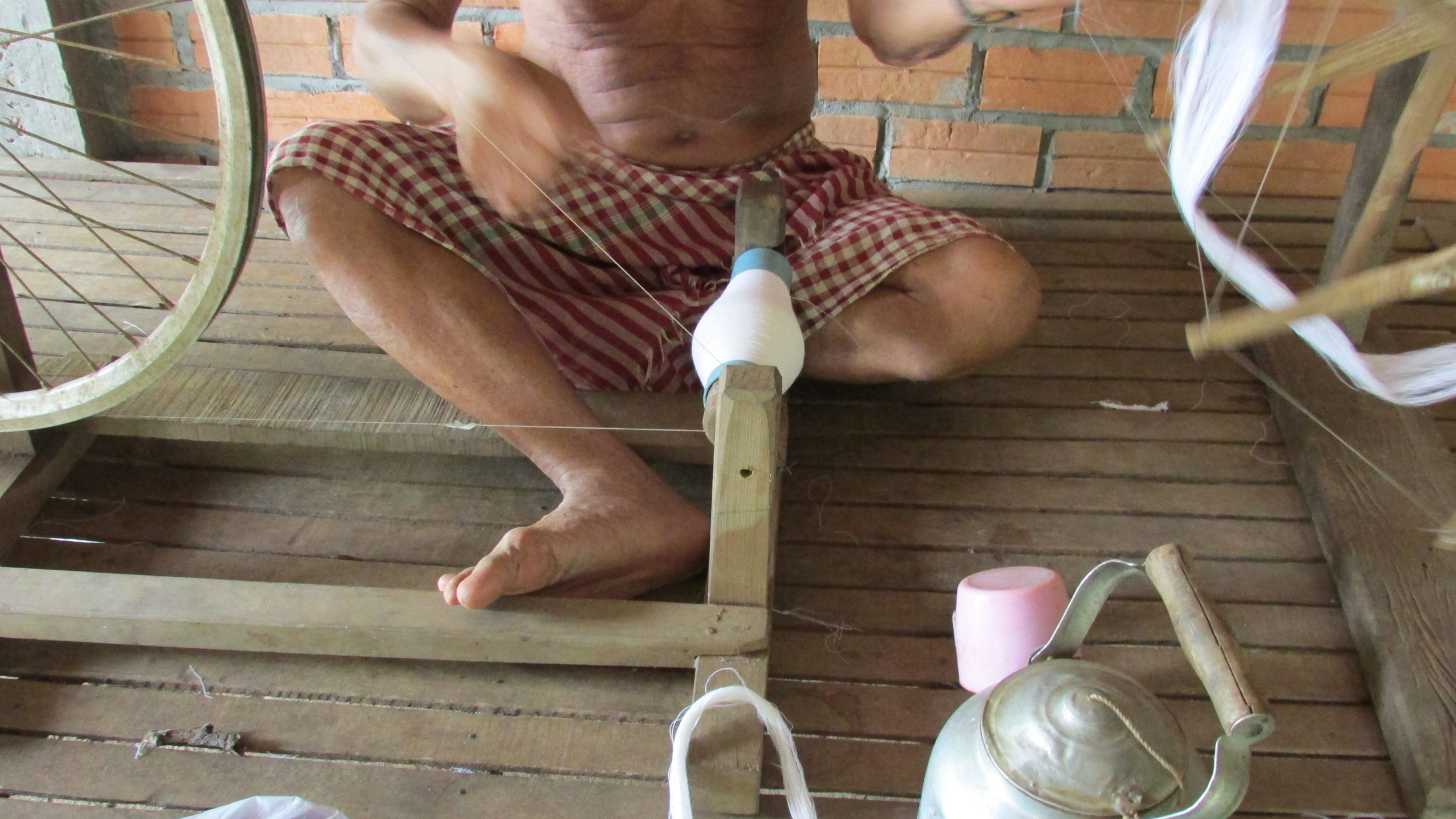 The krama weaver's husband, a retired teacher, spinning the cotton. He's wearing a krama, but he said his wife didn't make it. He got it as a gift from someone running for office.