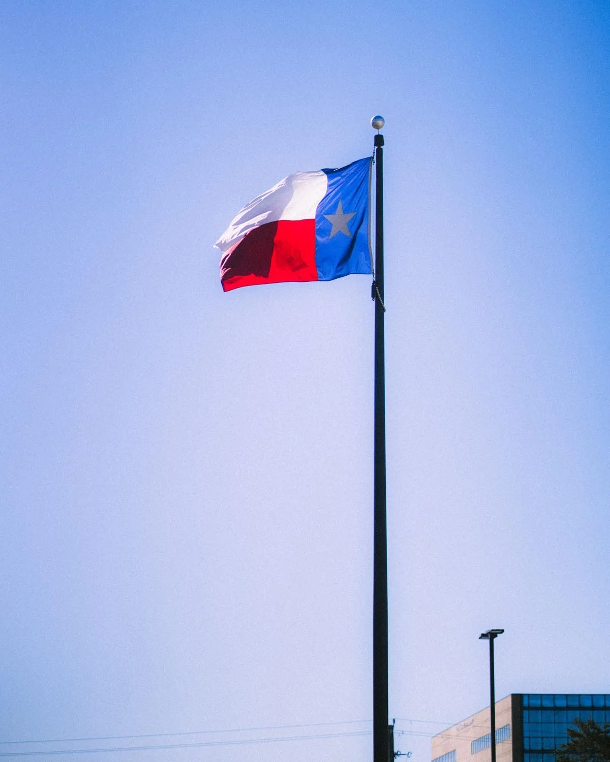 Flag of Texas flying on a flagpole against a clear blue sky.