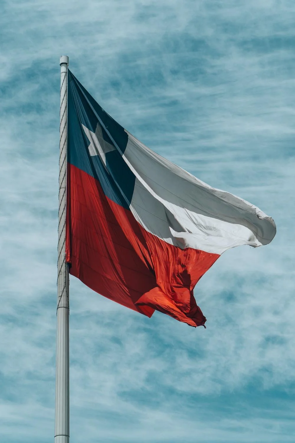 A flag with the design of the Texas state flag waving in the wind against a partly cloudy sky.