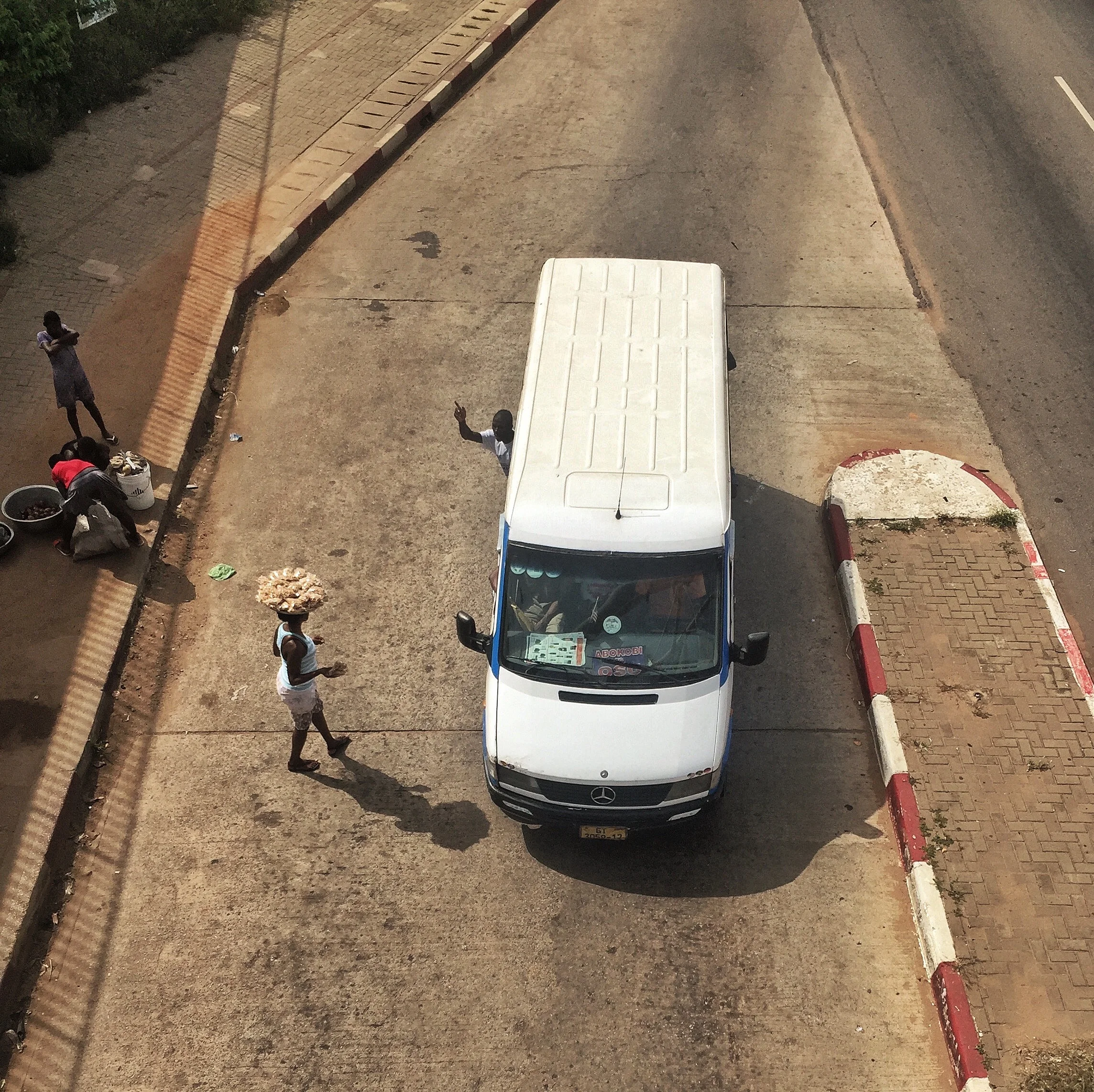 Street vendors sell goods to passengers in cars, trotros and bikes at red lights.