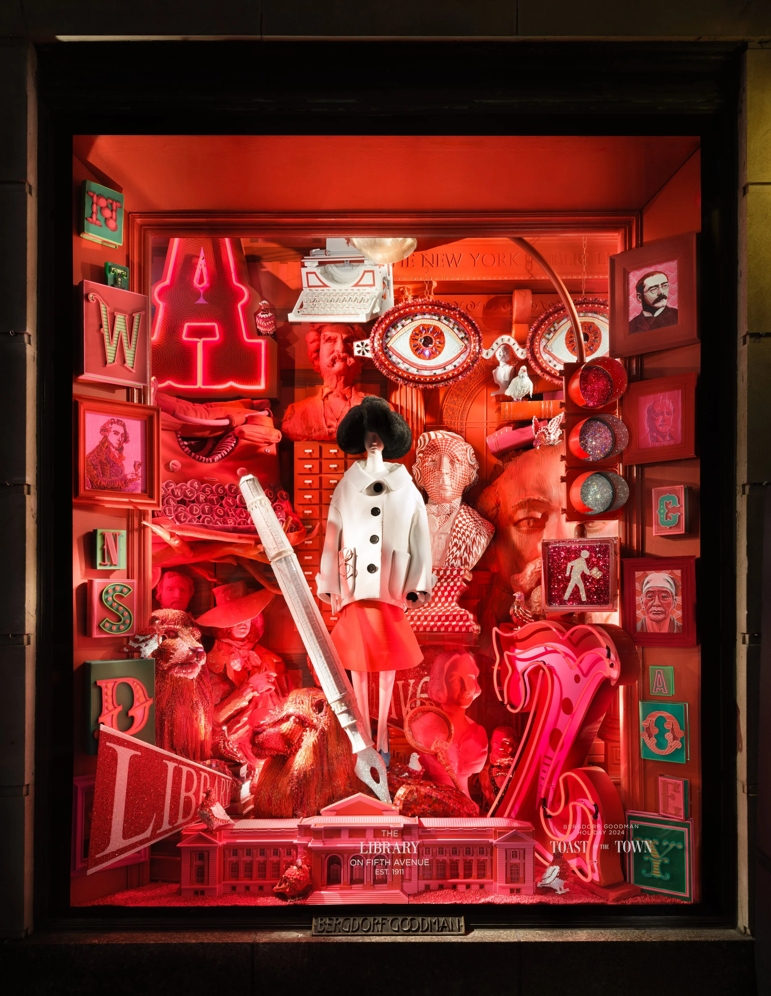 Colorful storefront window display with various pink, red, and white items including a mannequin, framed photos, a lion statue, neon signs, and decorative objects.