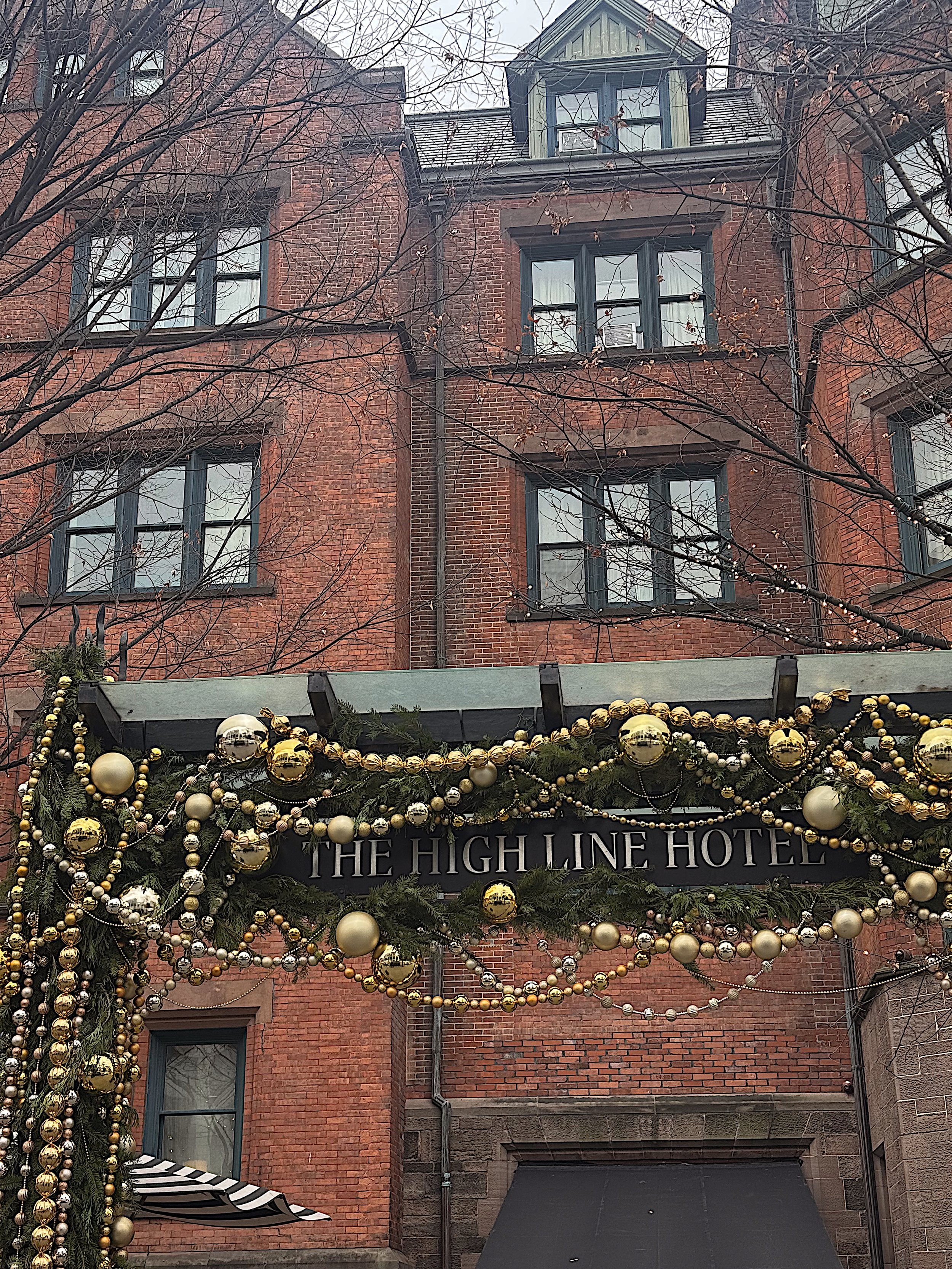 Exterior of The High Line Hotel decorated with Christmas ornaments and greenery, with a brick building and leafless trees in the background.